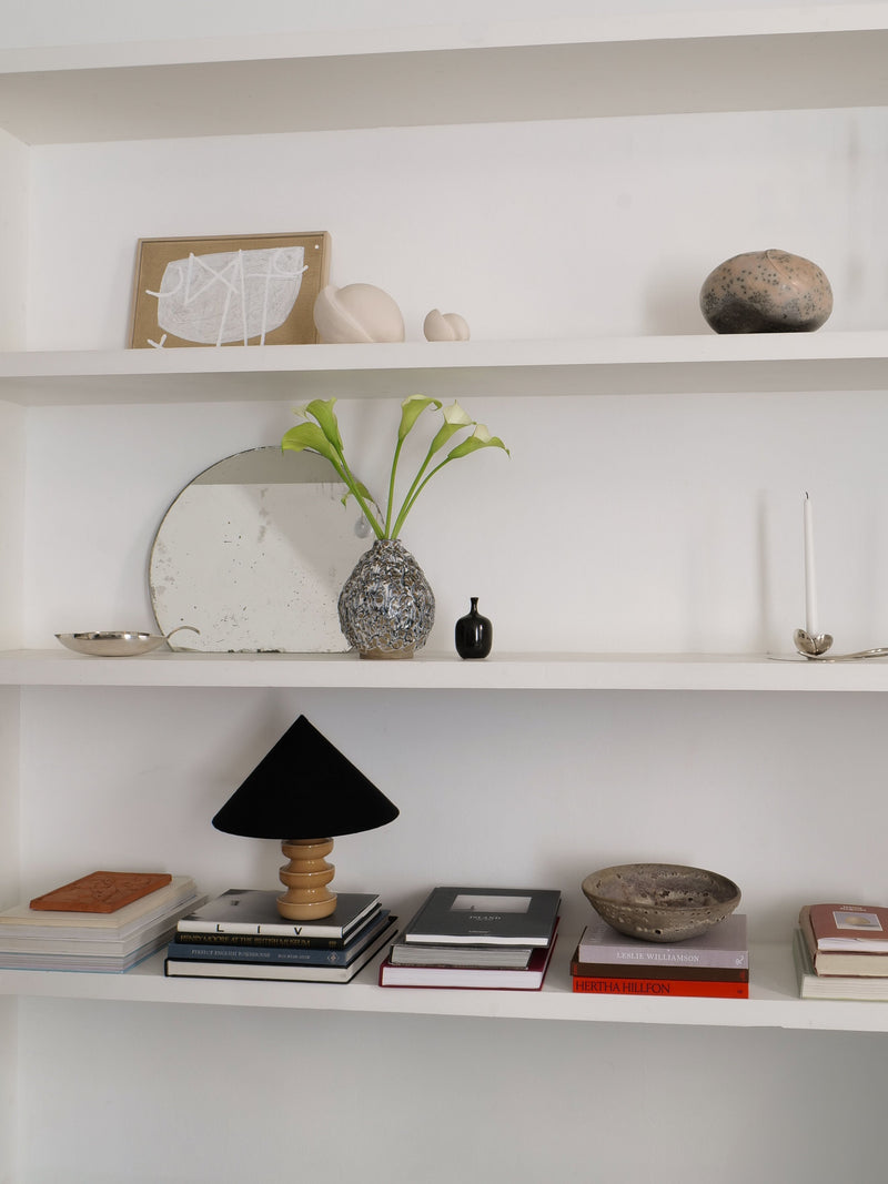 Black conical ceramic table lamp styled with books on white shelf