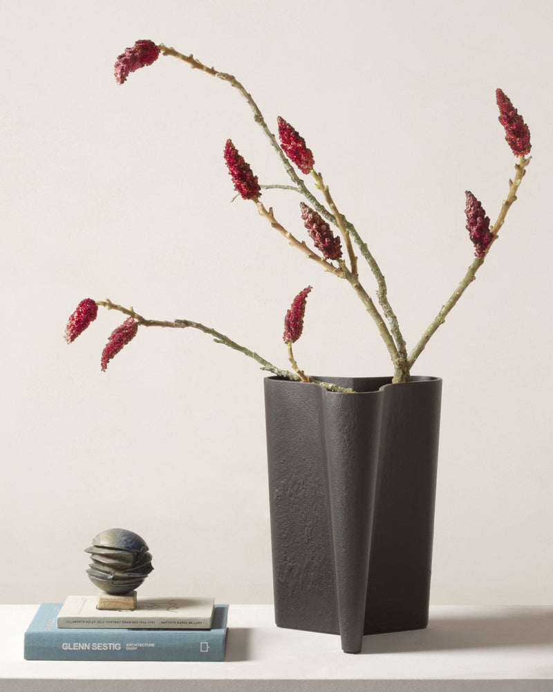 Tanell bronze vase with red flowering branches on white surface
