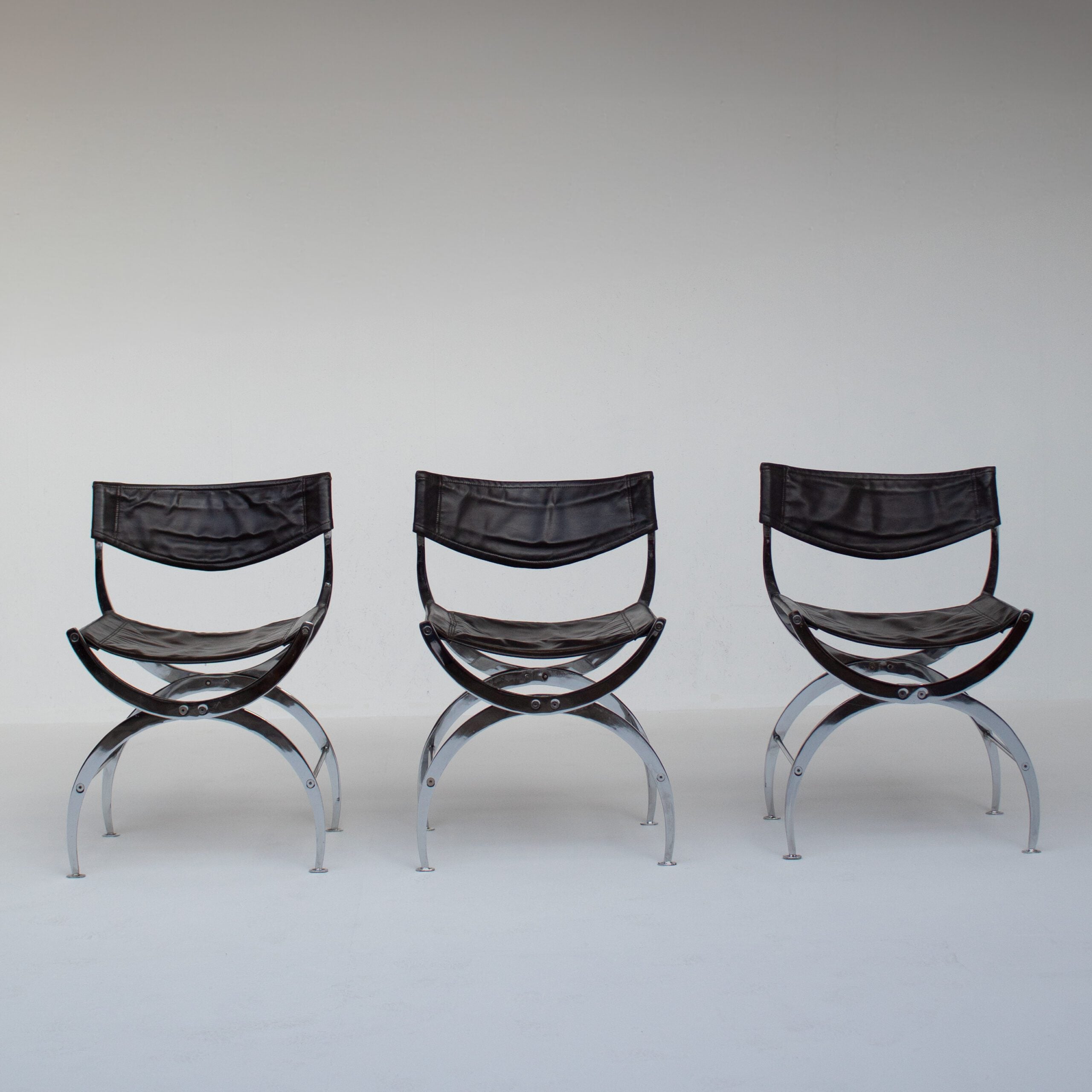 Set of 6 Italian Chrome Dining Chairs with Leather Seating — back view of three chairs in a minimalist setting