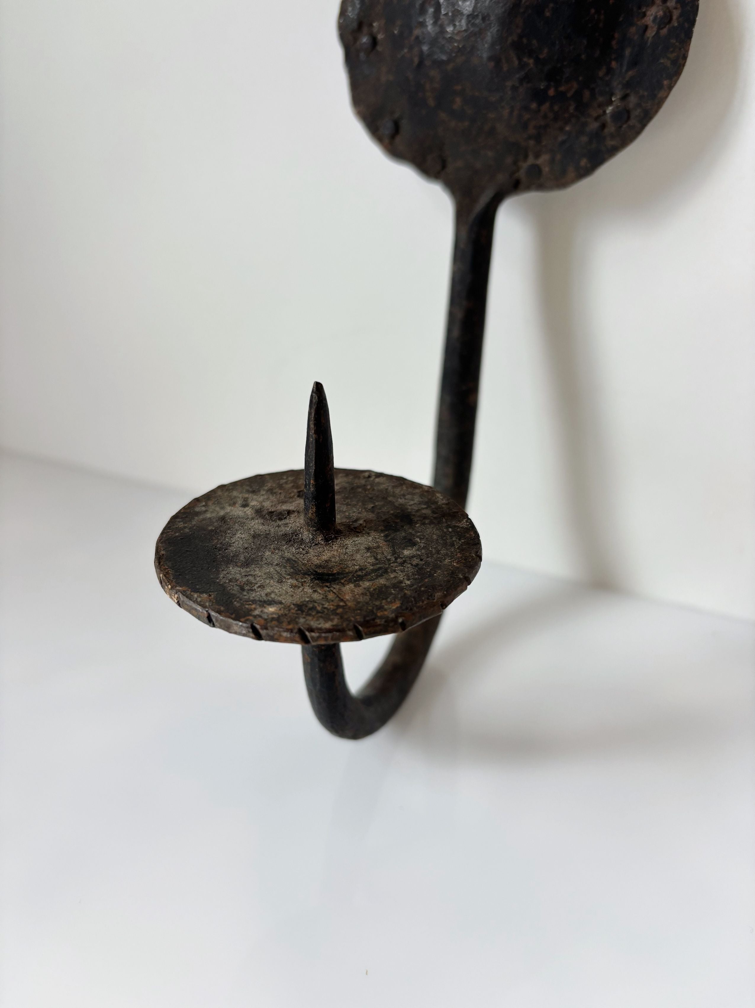 Hand-forged iron candleholder detail showing curved handle and spike