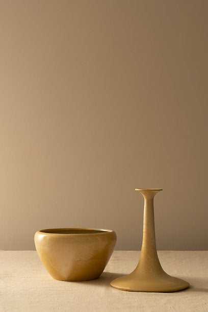 A hand-painted floral ceramic bowl and a matching candlestick on a beige cloth against a light tan background, evoking a minimalist and serene aesthetic, by Les Objets Amsterdam's Two-Piece Pot.