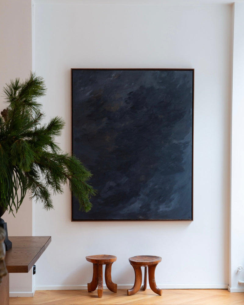 Nocturne" — dark abstract painting on white wall with wooden stools