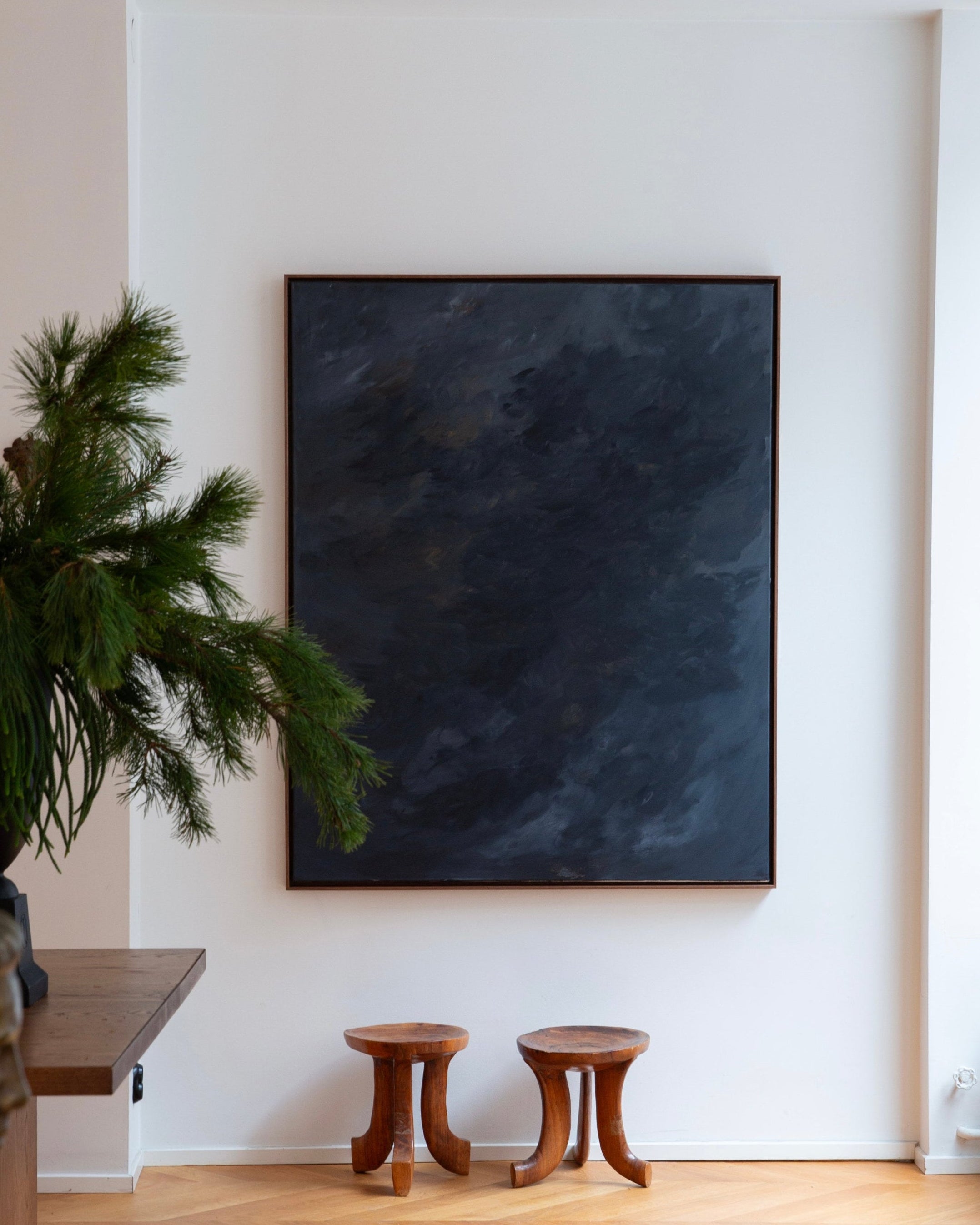 Nocturne" — dark abstract painting on white wall with wooden stools