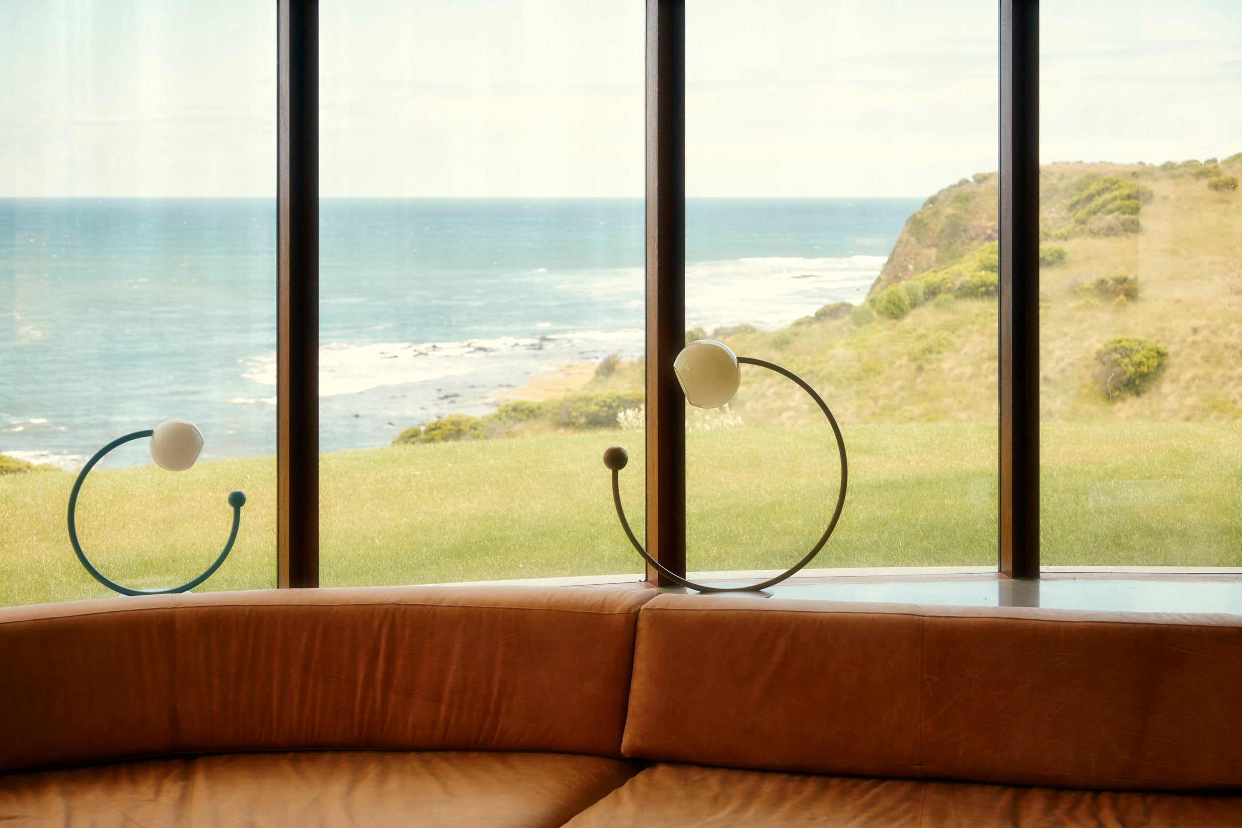 Oro Table Lamp w/ Handblown Glass — positioned on curved leather sofa with ocean view
