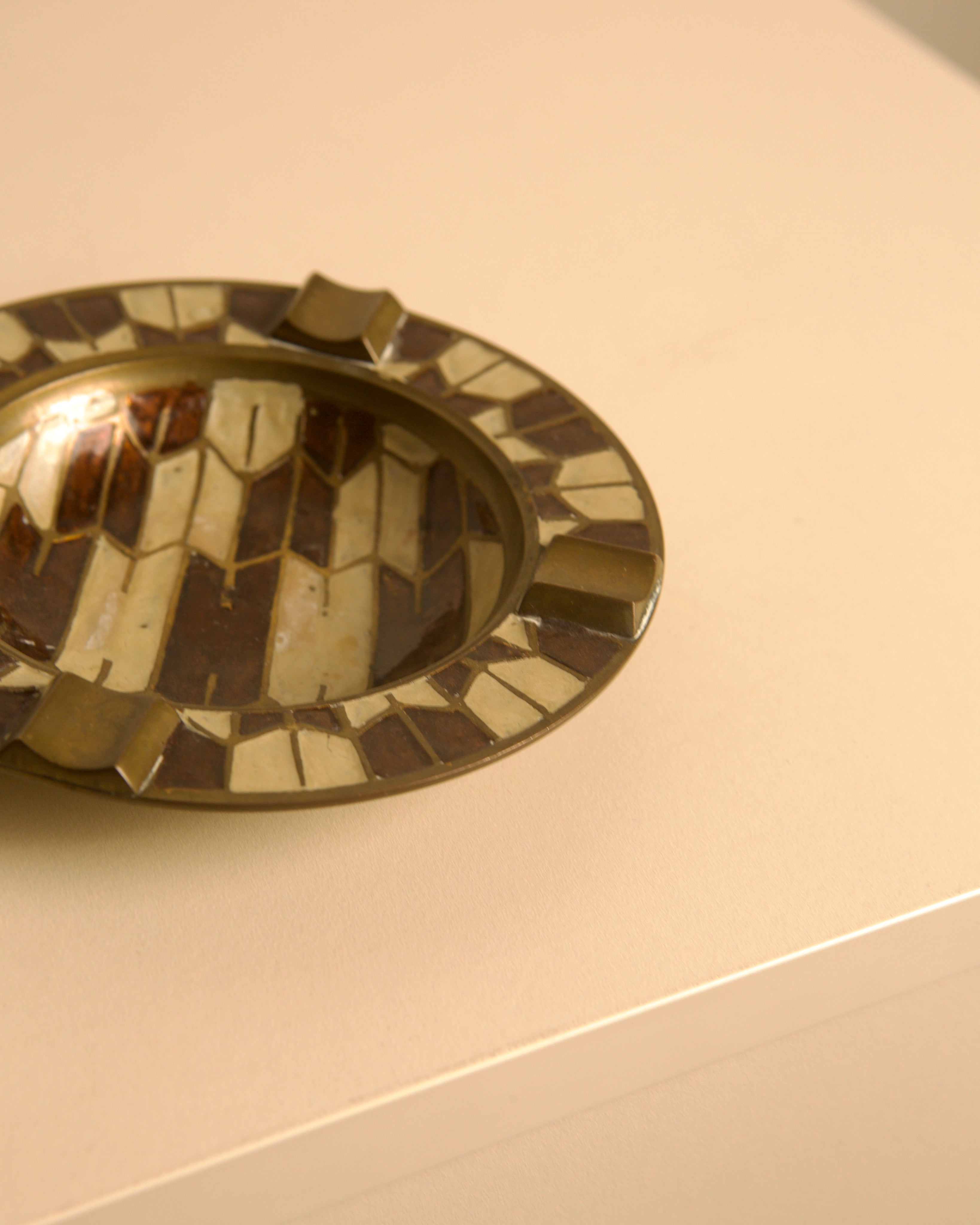 50's Brass Ashtray with Enameled Patterns — angled view on light surface
