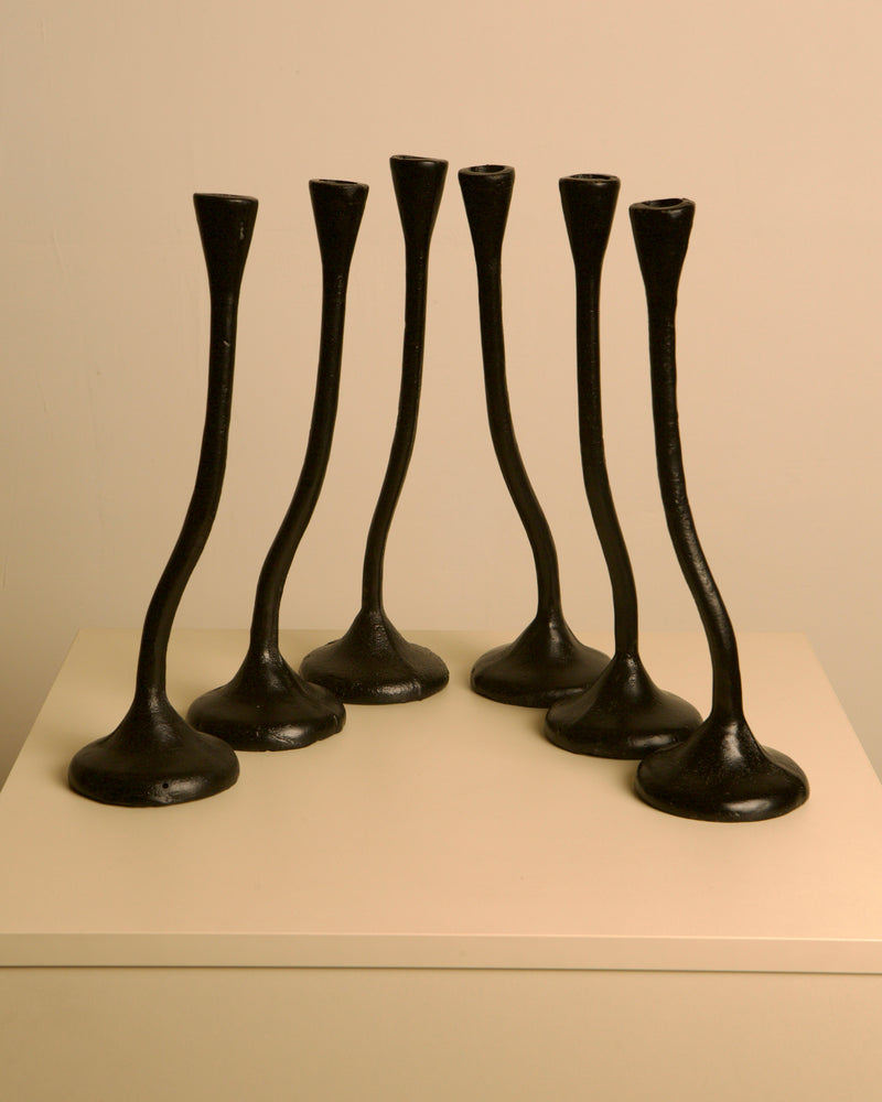 A set of 5 Treaptyque "Twisted" black cast aluminum candleholders from the 80s, featuring flared bases, is arranged on a light square surface against a plain beige background, showcasing sculptural design.