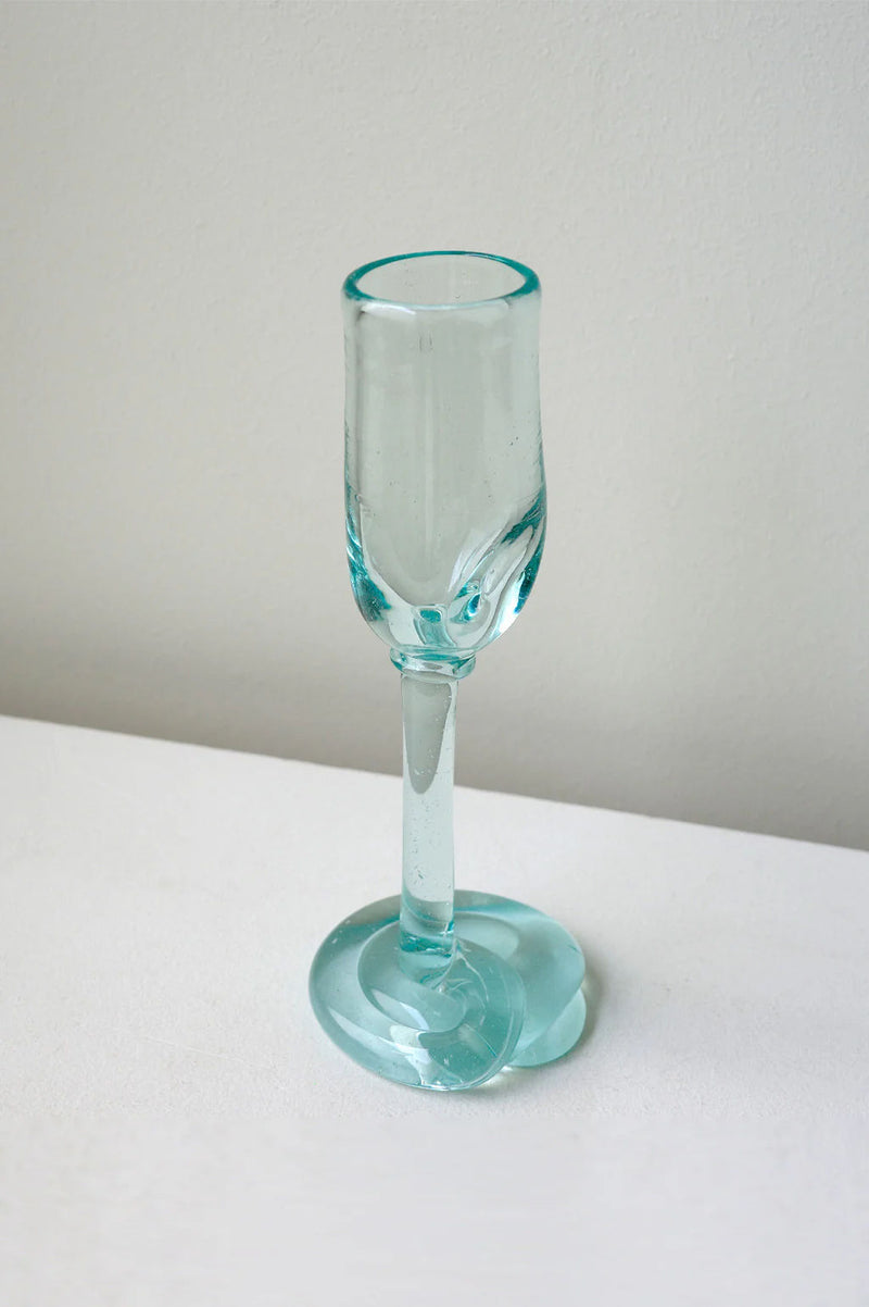 The Thaw - Recycled Flute Glass in Clear by Completedworks features a sculptural, melted-look base and sits elegantly on a white surface, showcasing contemporary glass artistry.