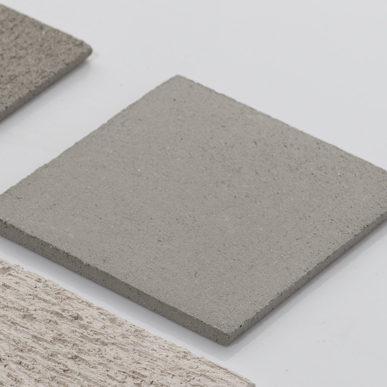 A close-up of three gray square tiles inspires sculptural designs—just like the Too 60-2 Table Lamps in Ceramic by Katia Langeard, ideal for elevating your bedside lighting.