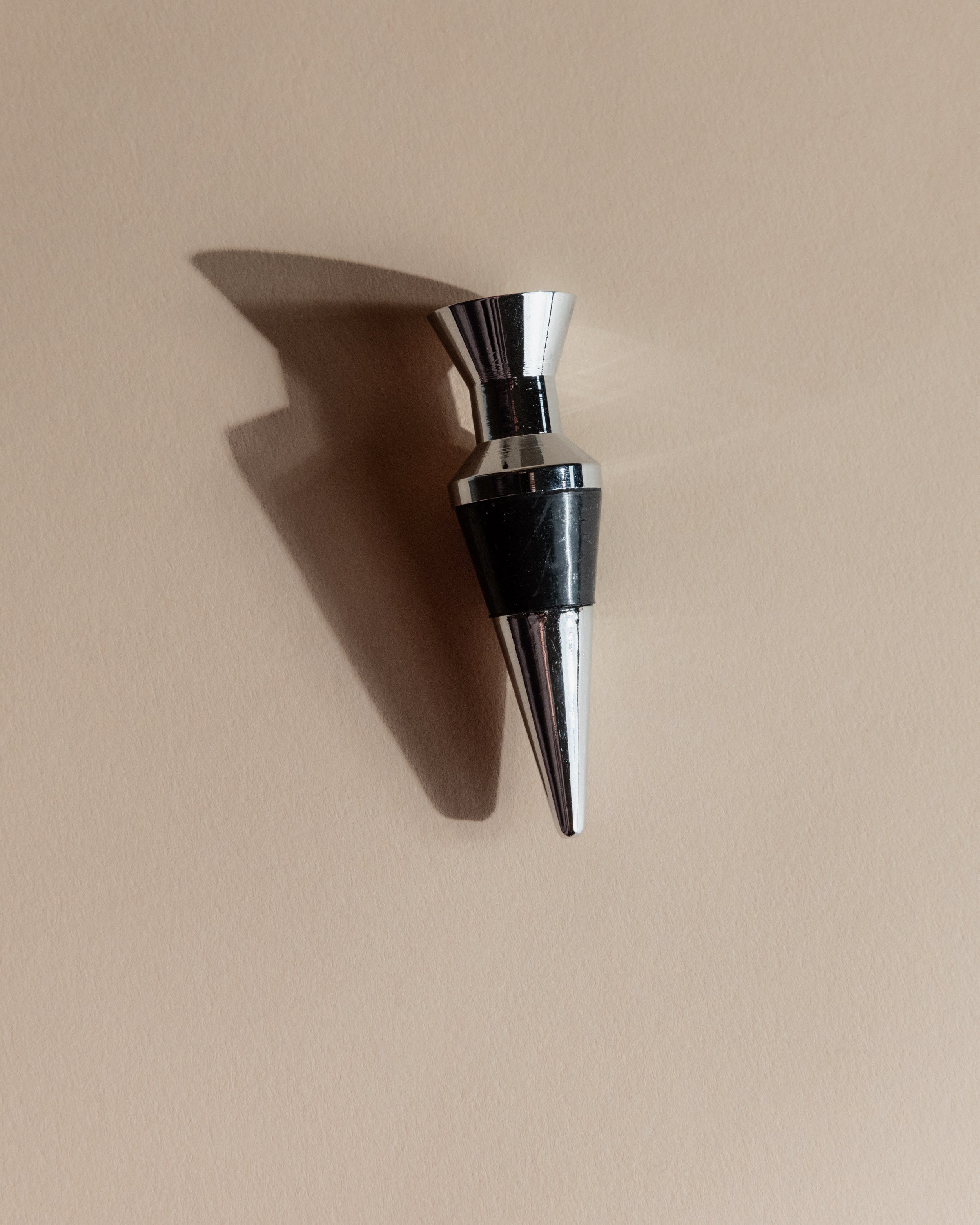 Vintage 1980s Bottle Stoppers Set of 2, Metal Geometric Conical Design Italy — top view of shiny metal stopper on beige backg