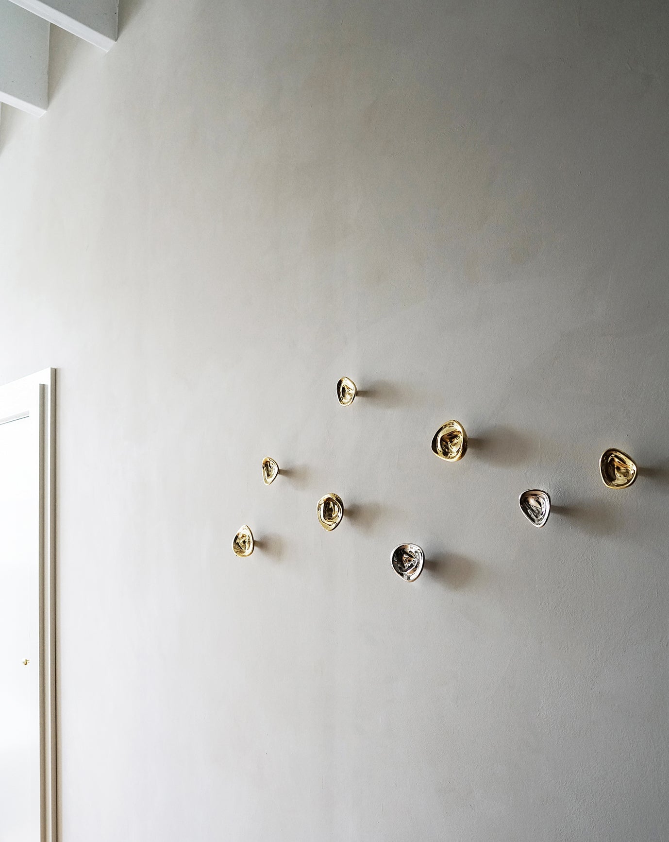 Ripple Hook - Small - Brass — arranged on textured wall in modern setting