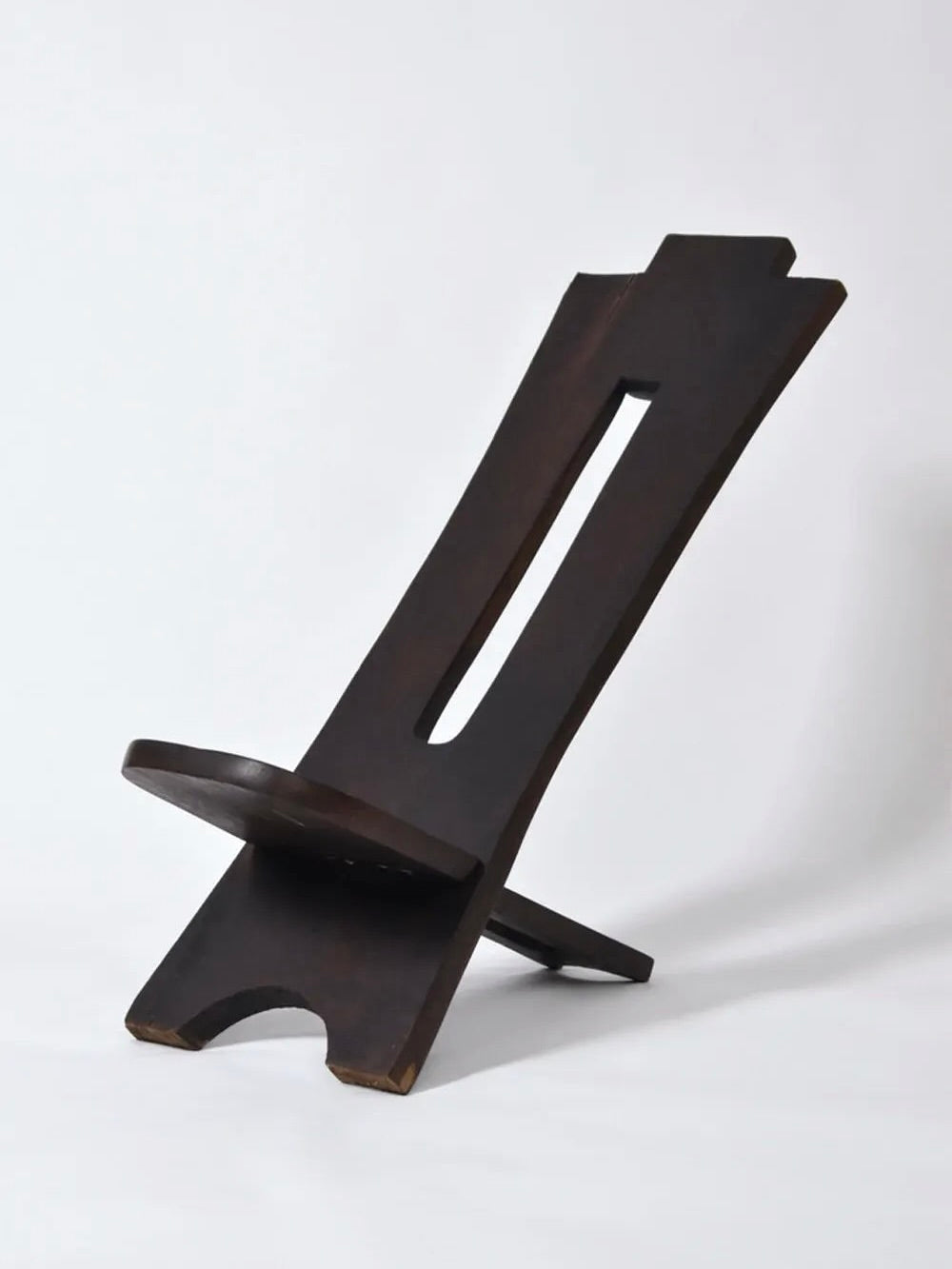 The Barracuda Interiors West African Wood Chair, 1960s, features a dark wood finish, slanted backrest, and central rectangular cut-out. Its minimalist design is inspired by classic West African styles. Shown against a white background.