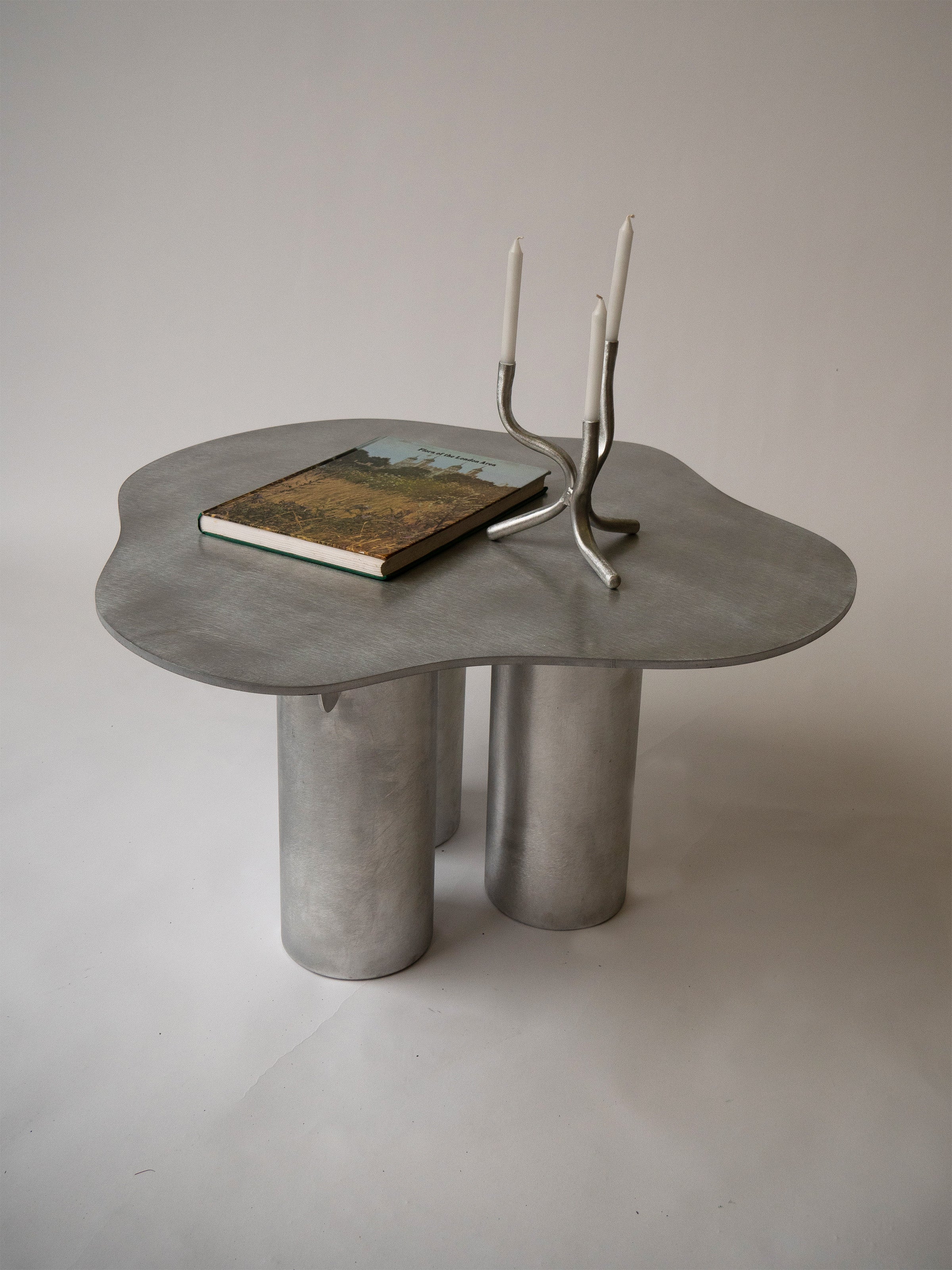 Aluminium Coffee Table — close-up of organic shape with book and candles
