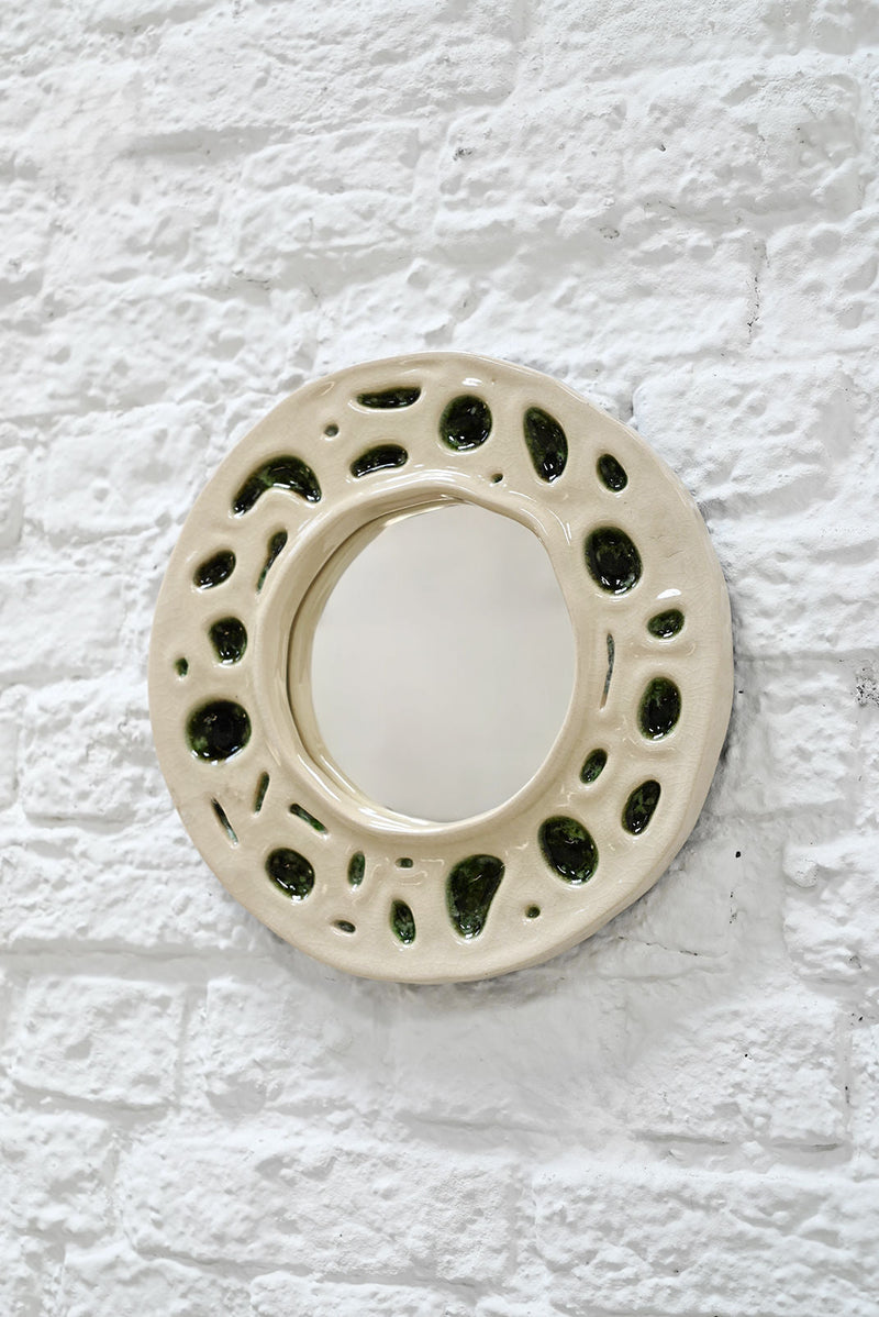 French ceramic mirror frame detail showing cream glaze with moss green organic cutouts