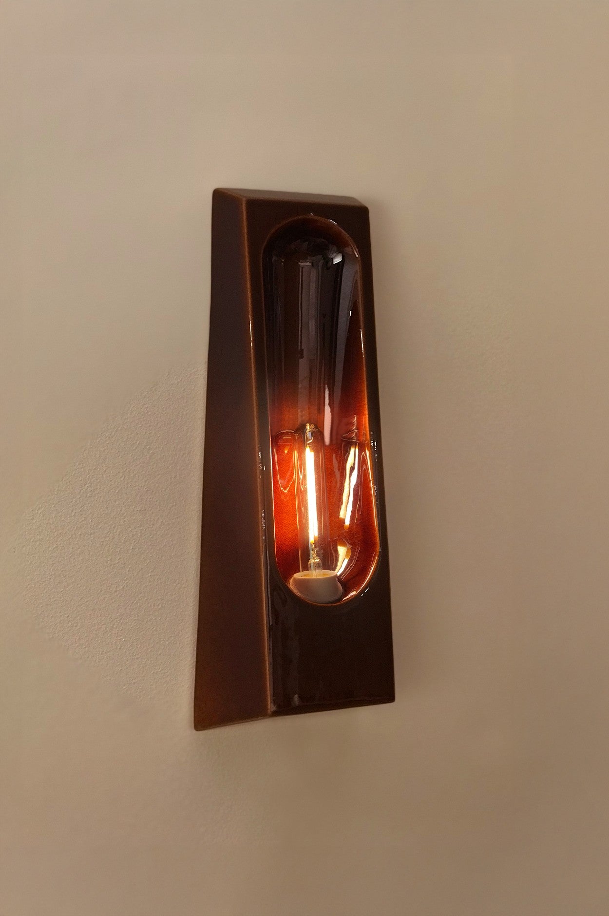 The Alcove Porto by Violaine d'Harcourt is a modern, wall-mounted sconce with a glossy brown ceramic finish and an exposed vertical bulb—ideal for elegant interior lighting.