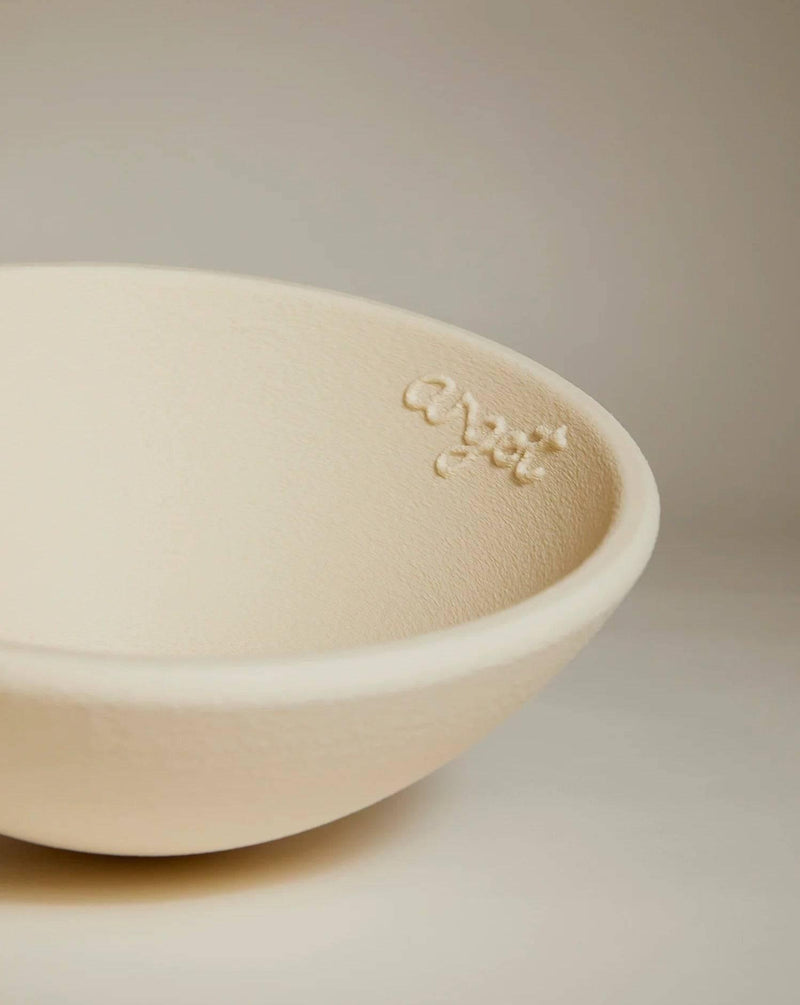 Against a neutral background, the Acorn Bowl Grand by Argot Studio—a cream-colored, sculptural ceramic piece with a gently curved rim—is featured. The word "alysi" is elegantly inscribed inside near the edge, accentuating its handcrafted artistry suitable for luxury interiors.