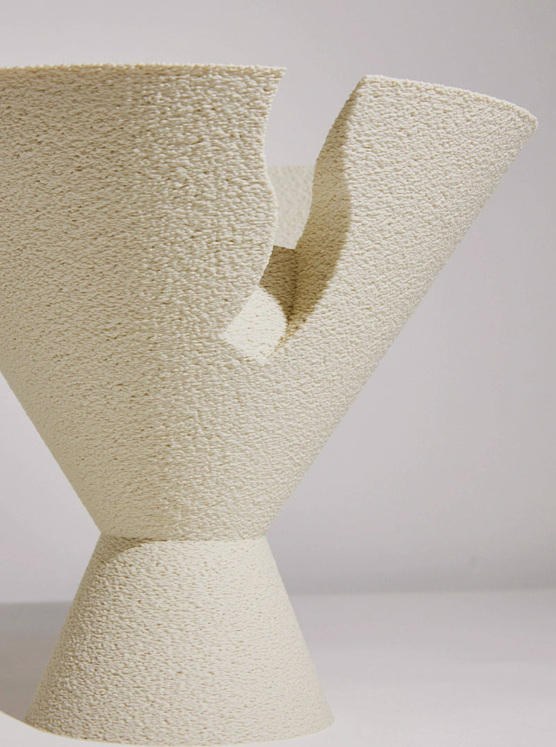 A close-up of a textured, modern sculptural Tyro Bowl created using 3D printing technology by Argot Studio, with an irregular top and conical base on a neutral background. The surface appears rough, resembling a.