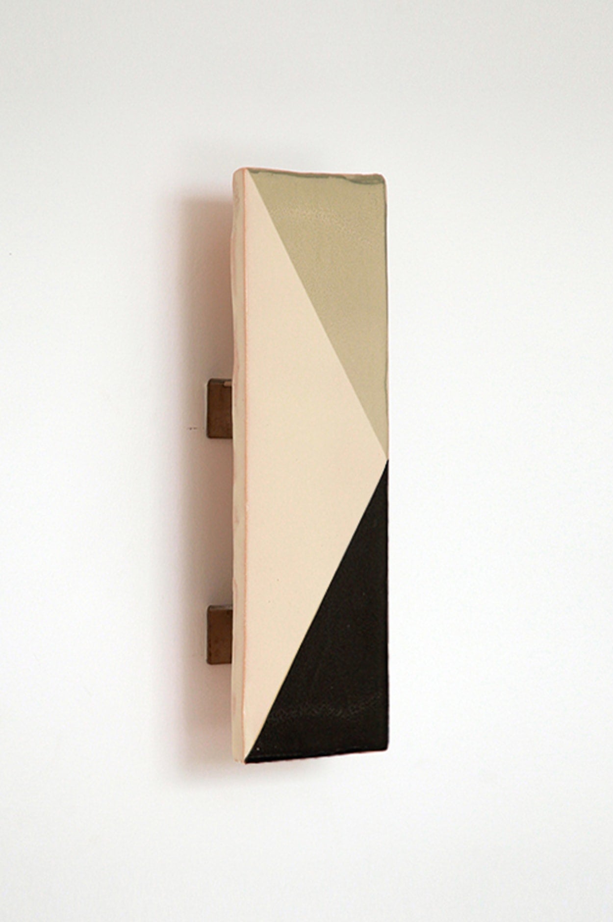 The Tile VN by Violaine d'Harcourt is a rectangular ceramic wall piece with a geometric design in beige, cream, and black triangles, mounted vertically against a plain white background.