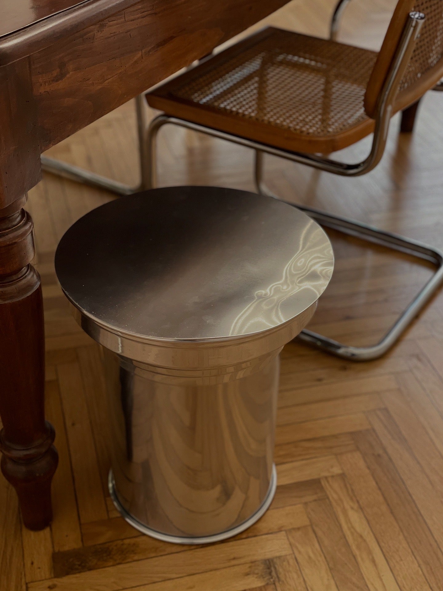 Art Deco Side Table - Mirror-Polished Metal Collection — angled view beside wooden dining table