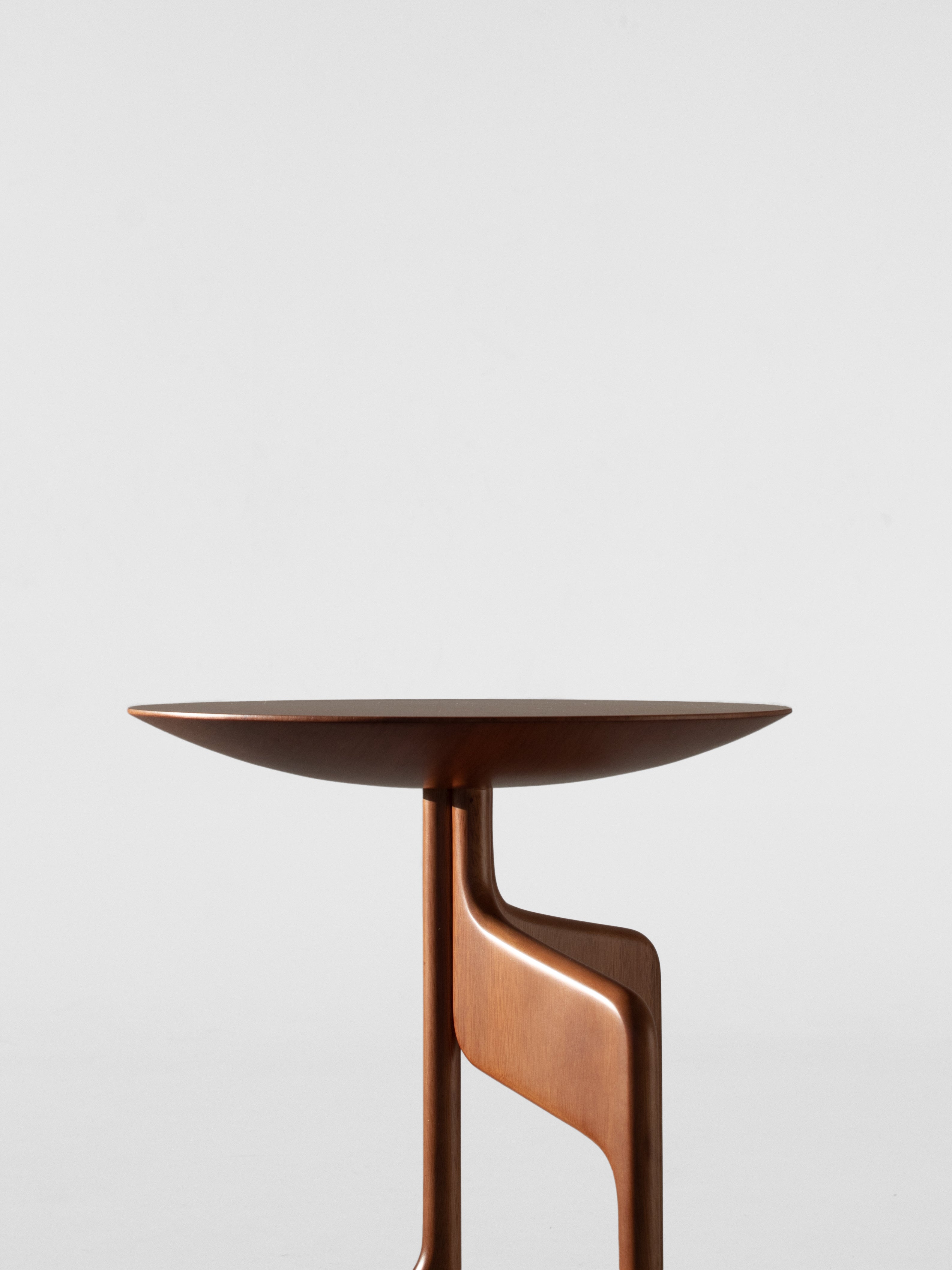 The "Vereda" Side Table by Luciano Costa Estúdio is a modern, round piece from the Nômade collection, featuring a smooth top and sculptural base in solid lyptus wood, shown against a plain white background.