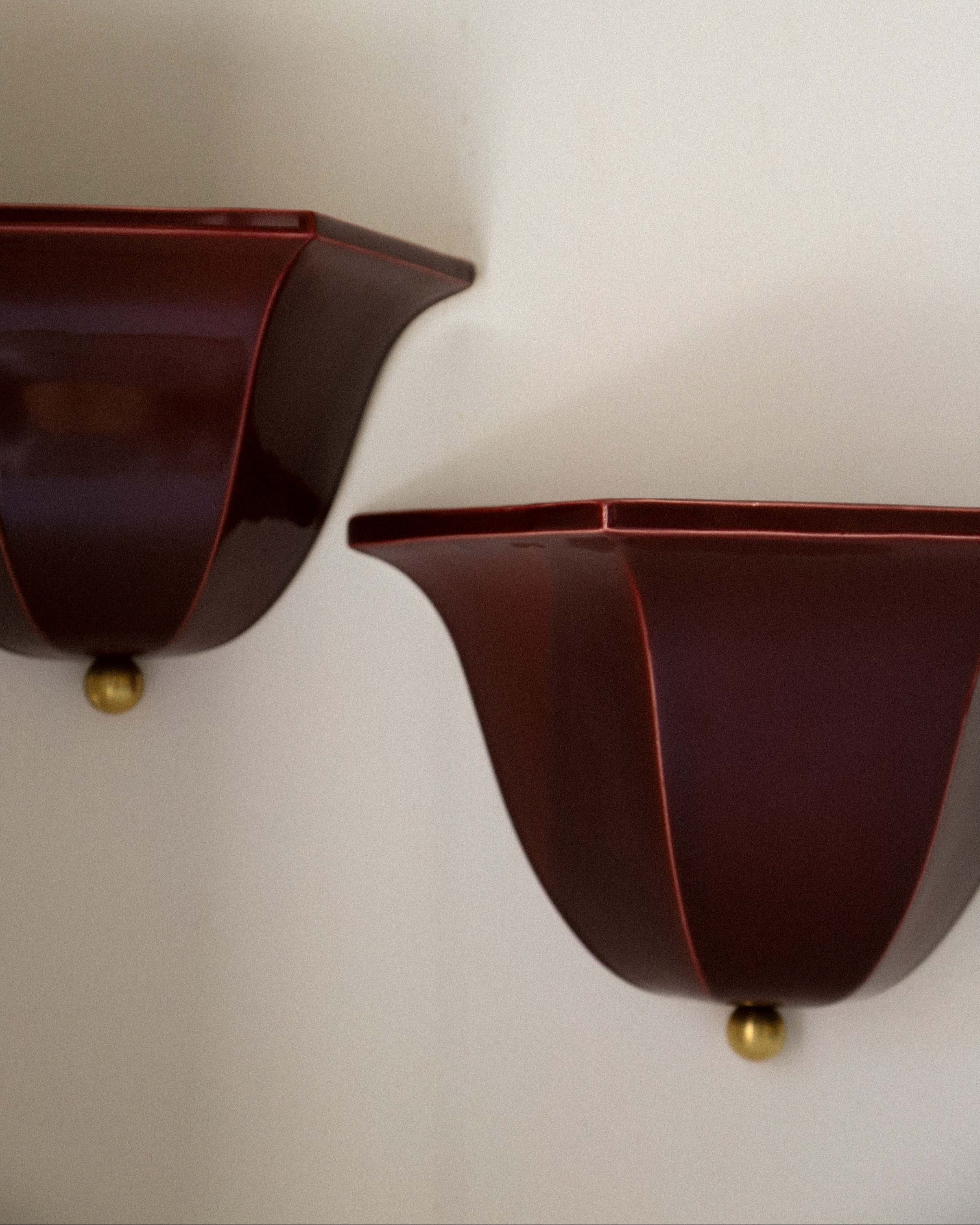 Two burgundy glass Maeve wall sconces with brass ball details