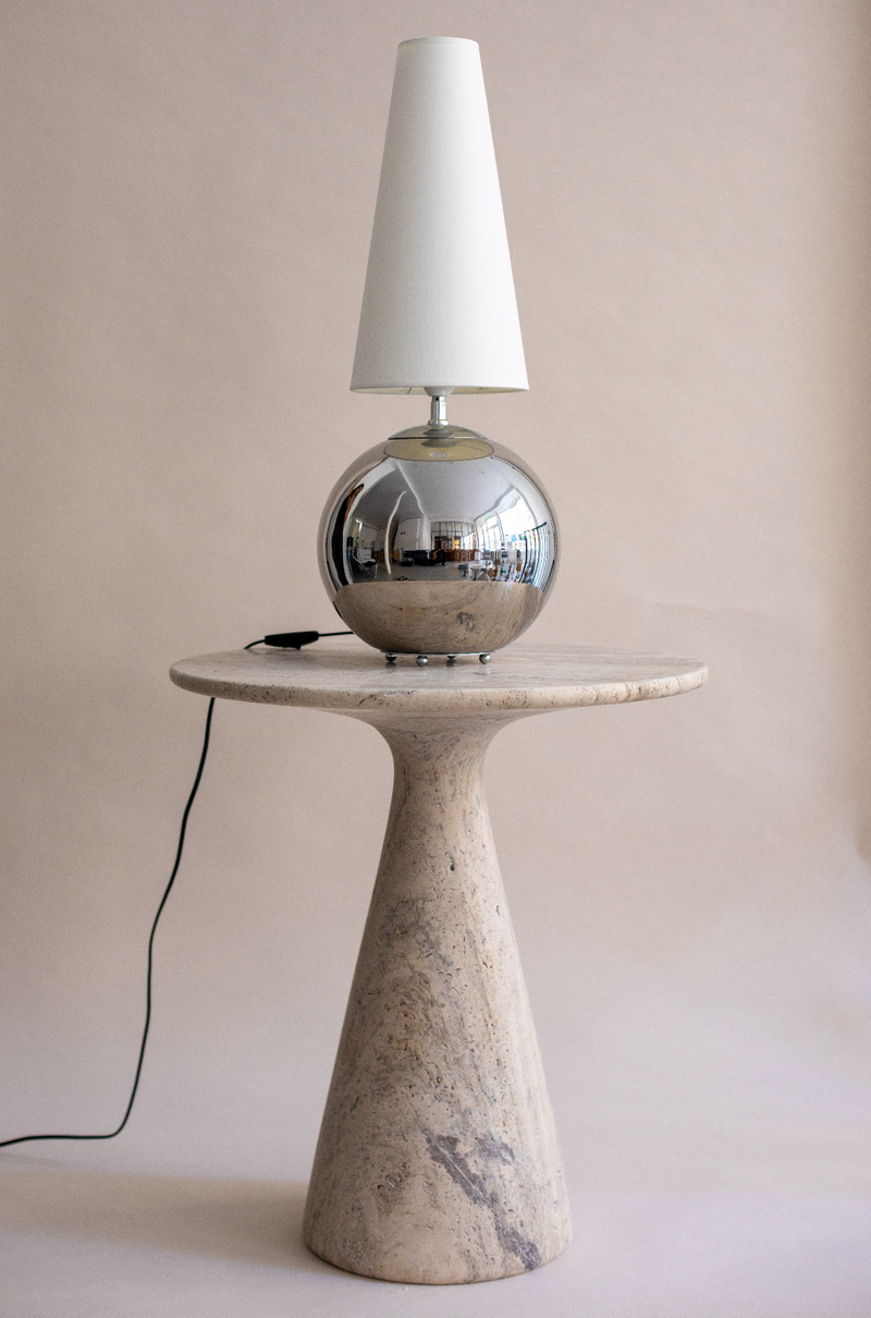 Chrome spherical table lamp with white shade on travertine pedestal