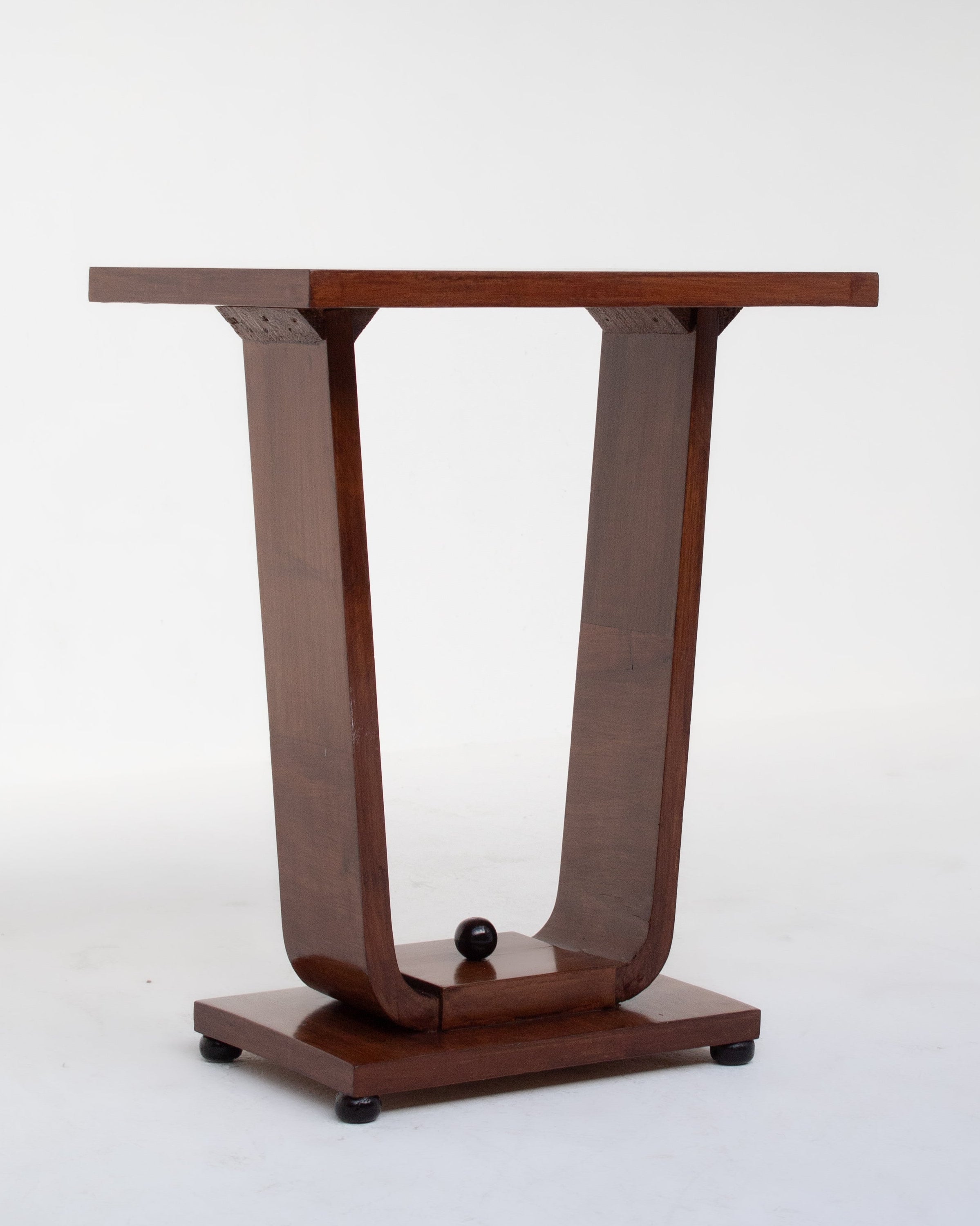 The Low Art Deco Side Table by Malata Antwerp features a modern, minimalist wooden design with a narrow rectangular top, U-shaped curved supports, and a decorative sphere on the base inspired by subtle Art Deco influences.