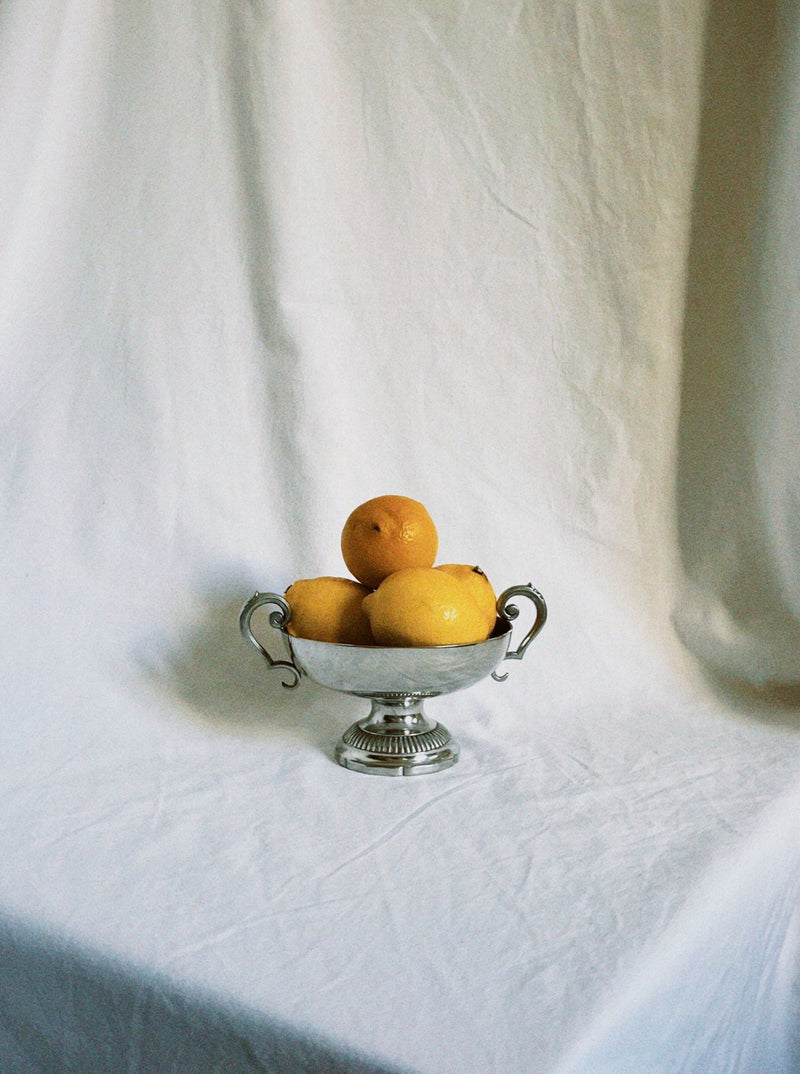 Silver footed fruit bowl with ornate handles holding oranges