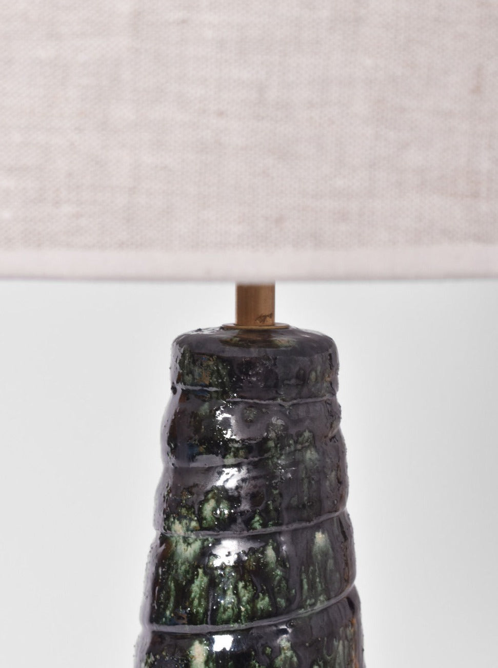 Close-up of the "Teotihuacan" Green Ceramic Table Lamp, Barracuda Edition by Barracuda Interiors, featuring a green glazed base inspired by Teotihuacan artistry and topped with a beige fabric shade against a light, plain background.