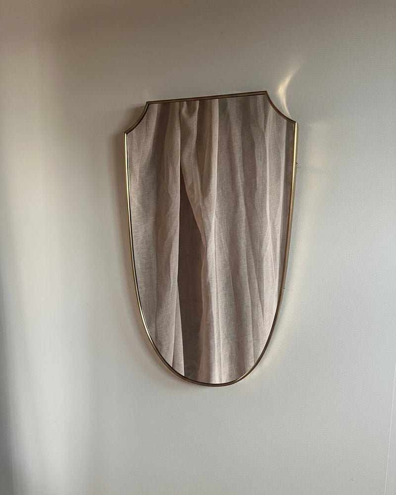 Mid-century Italian brass shield mirror with curved frame on white wall