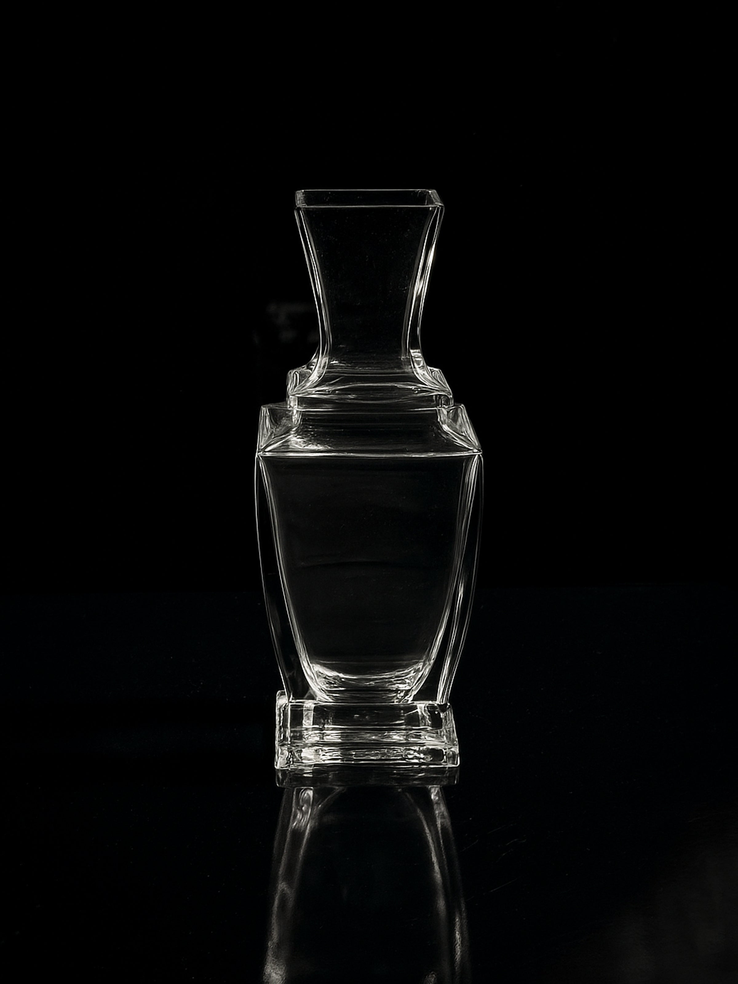 The Vintage Baccarat Art Deco Vase - 1980s by Dodo Vintage, featuring a square base and narrow neck, is displayed empty against a black backdrop, casting a subtle reflection that highlights its elegant design.