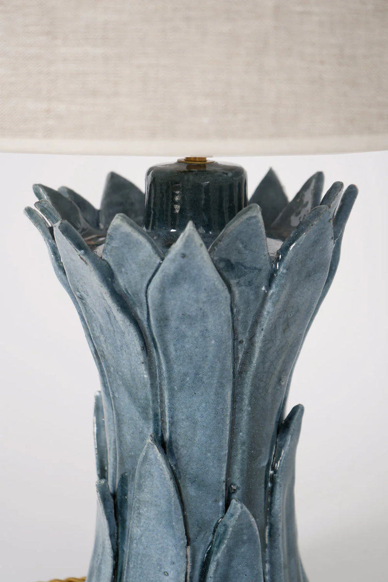 Close-up of Barracuda Interiors' "Sintra" Blue Table Lamp, featuring overlapping blue ceramic leaves handcrafted in Portugal, with a partially visible light beige fabric lampshade at the top of the image.