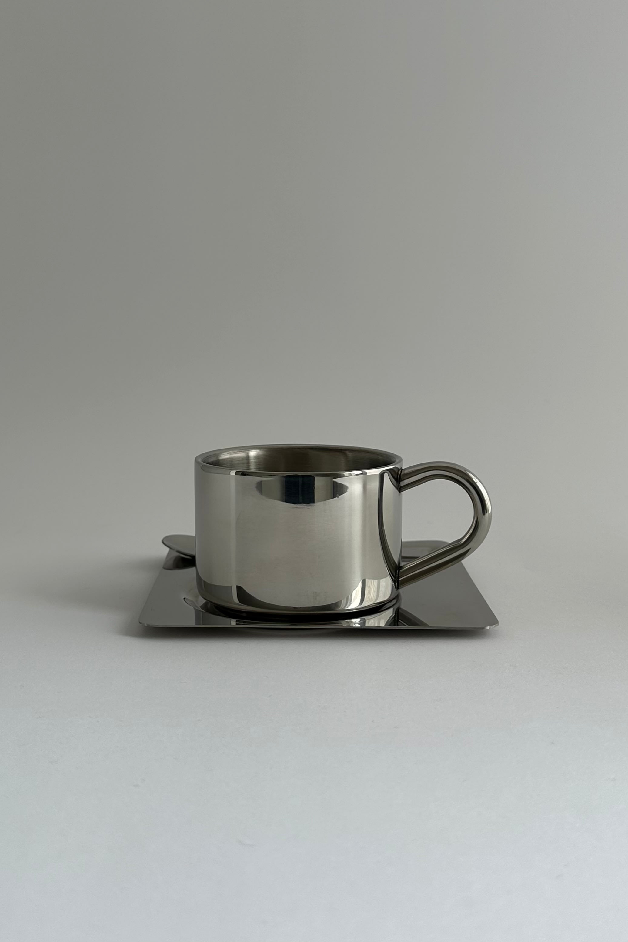 'HEDONISM' stainless steel cup with saucer — close-up