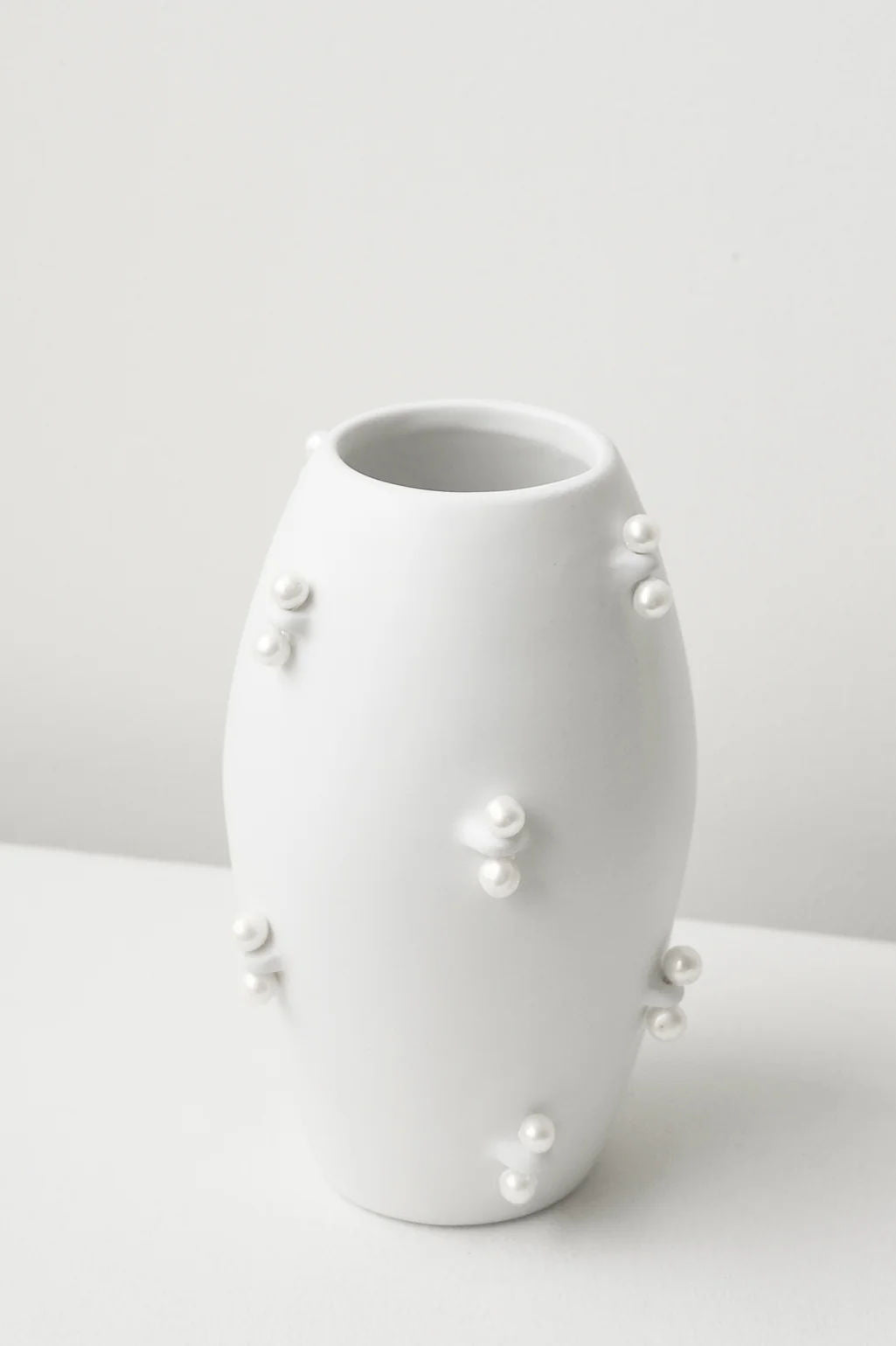The Pinched - Small Vase In Matte White by Completedworks features a smooth ceramic body with a matte finish and clusters of raised, pearl-like accents—an elegant decorative piece for any setting.