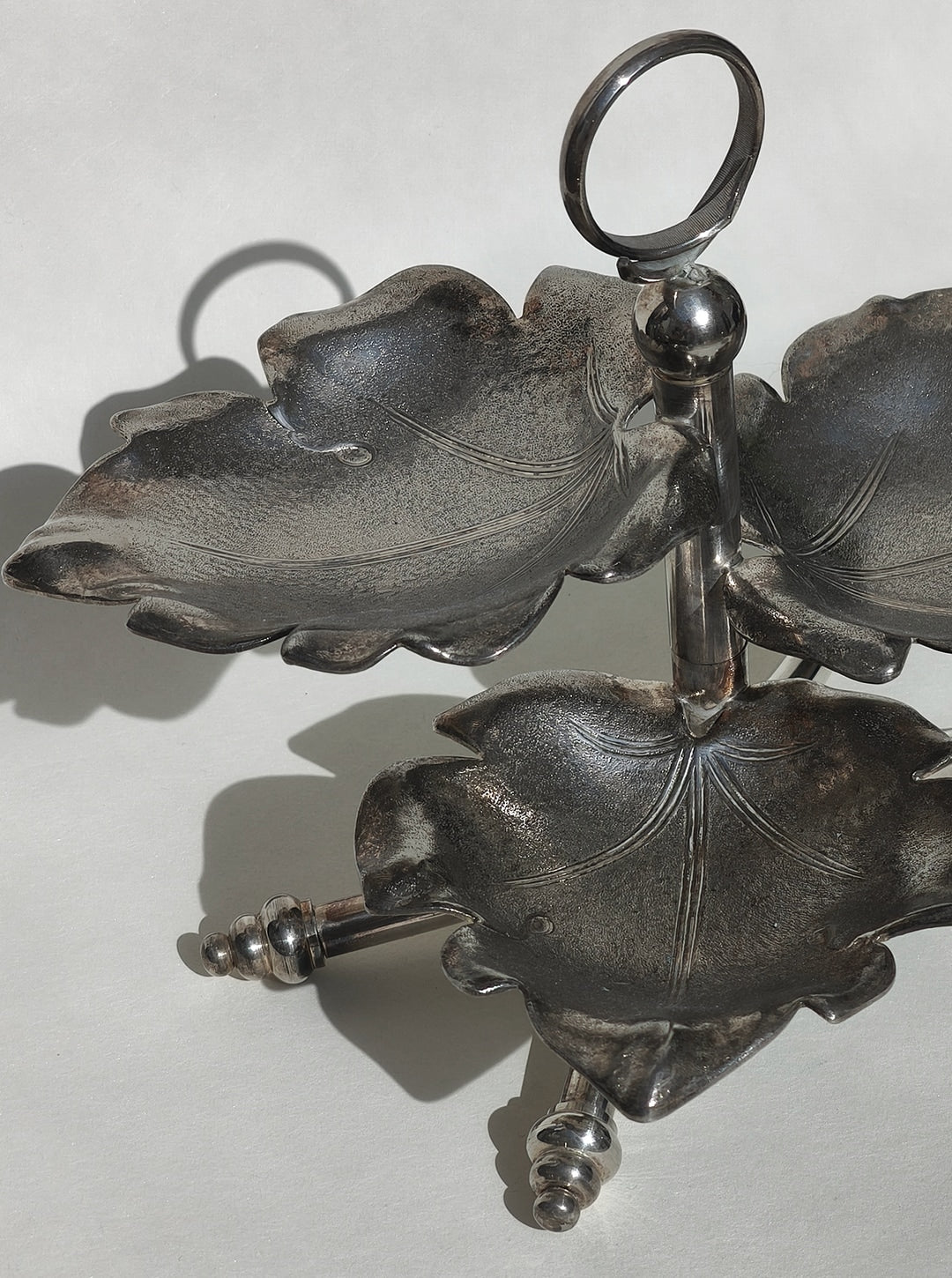 Three-tier leaf-shaped serving tray in dark metal with chrome stand