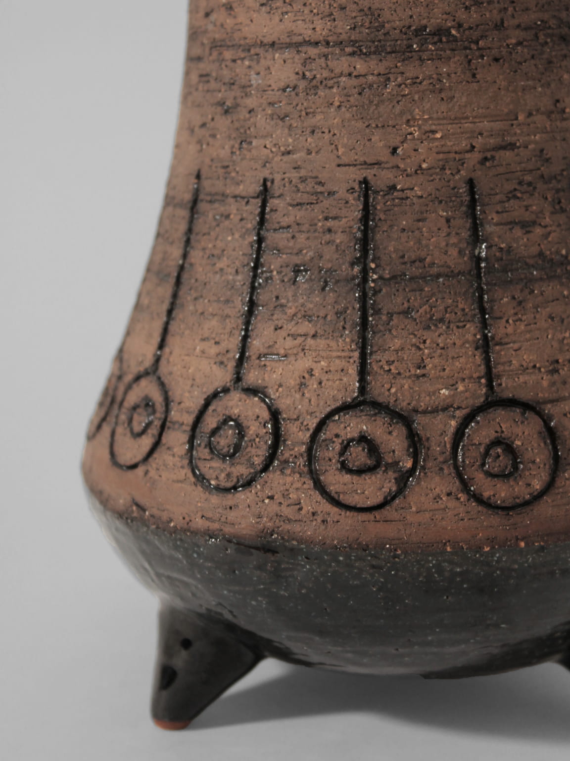 A close-up of the Eke Bjerén Ceramic Vase On Legs for Gabriel, Sweden, 1960s by Vintage Stories—this textured brown faience vessel features circular patterns, black vertical lines, and stands on small pointed legs.
