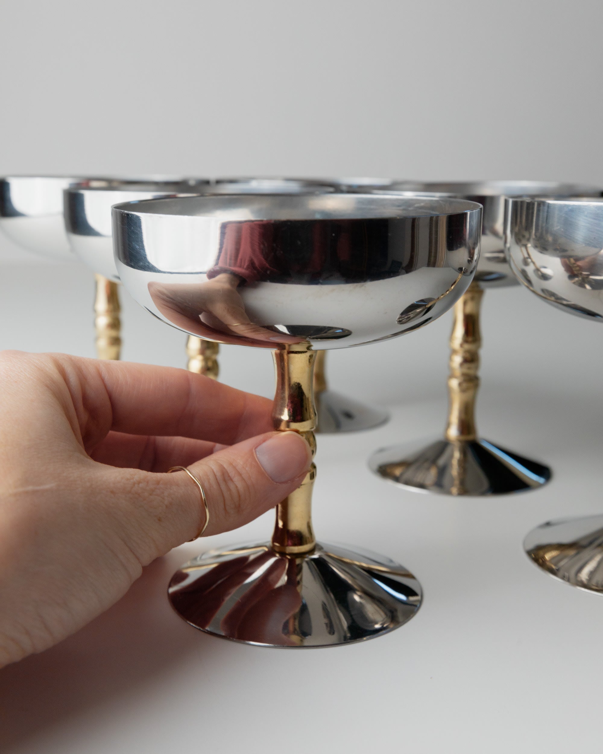 6 Stainless Steel Champagne Coupes 70s — hand holding coupe with gold stem