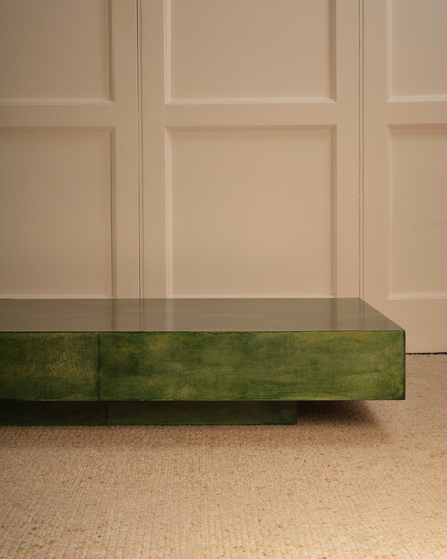 The Green parchment table by Galerie Vauvart, a minimalist Italian design, sits on a beige textured carpet against cream paneled walls.
