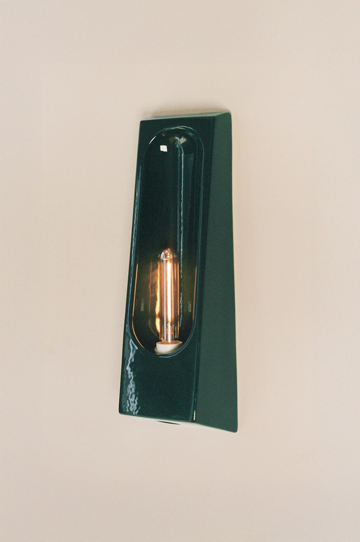 The Alcove Verde wall sconce by Violaine d'Harcourt features a glossy dark green angular frame and an exposed vertical Edison bulb, creating elegant éclairage intérieur when mounted on a light-colored wall.