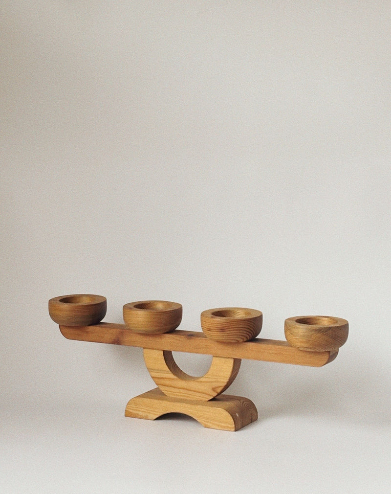 The Large Pine Candelabra by Stig Johnsson for Huerto features four round holders on a horizontal beam with a curved, rectangular base, all crafted in wood, and is inspired by Nordic mid-century design.