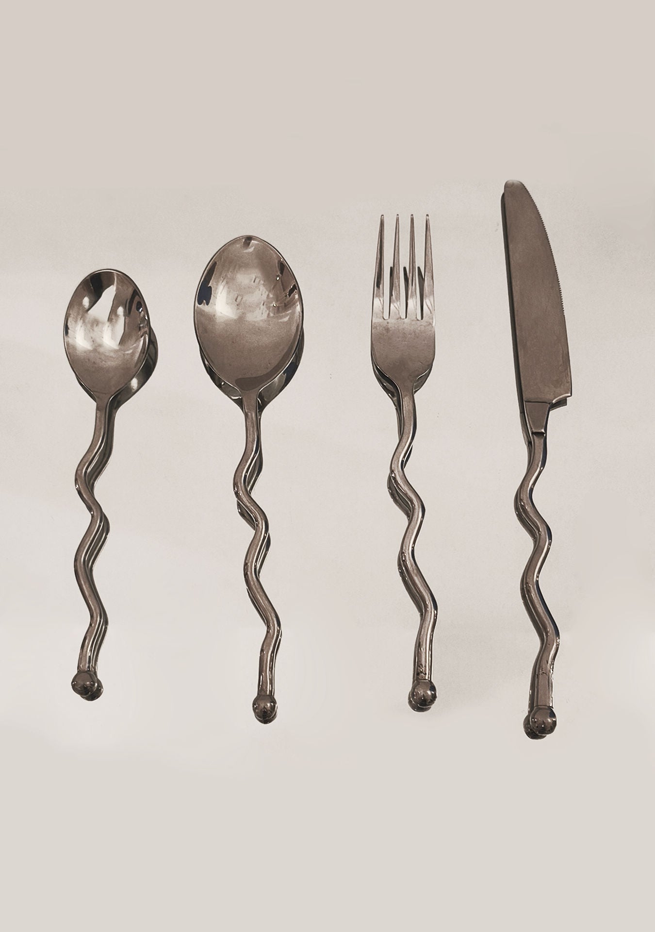 The Les Objoies Set of 4 Zig-zag Cutlery—teaspoon, tablespoon, fork, and knife—features wavy handles and is displayed vertically against a light background.