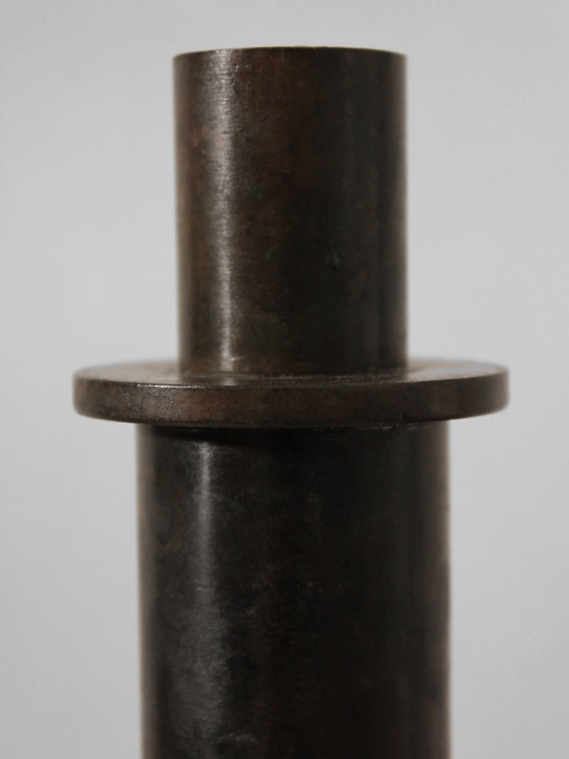 A close-up photo of a Pair of Brutalist Massive Iron Candle Holder by Vintage Stories, 1970s, featuring dark metal cylinders with wide flat rings, set against a plain light gray background.