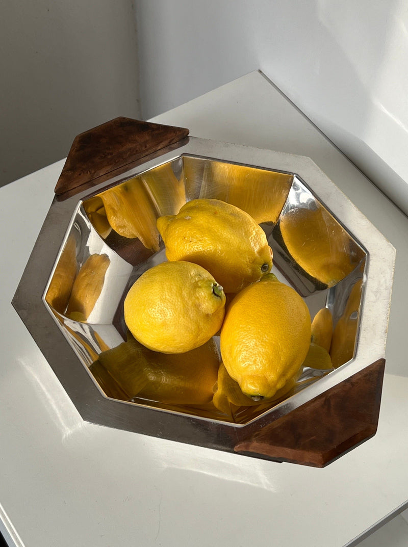 The Manushi Art Deco Decorative Dish, silver and octagonal with wooden handles, holds four yellow lemons on a white surface in bright natural light.