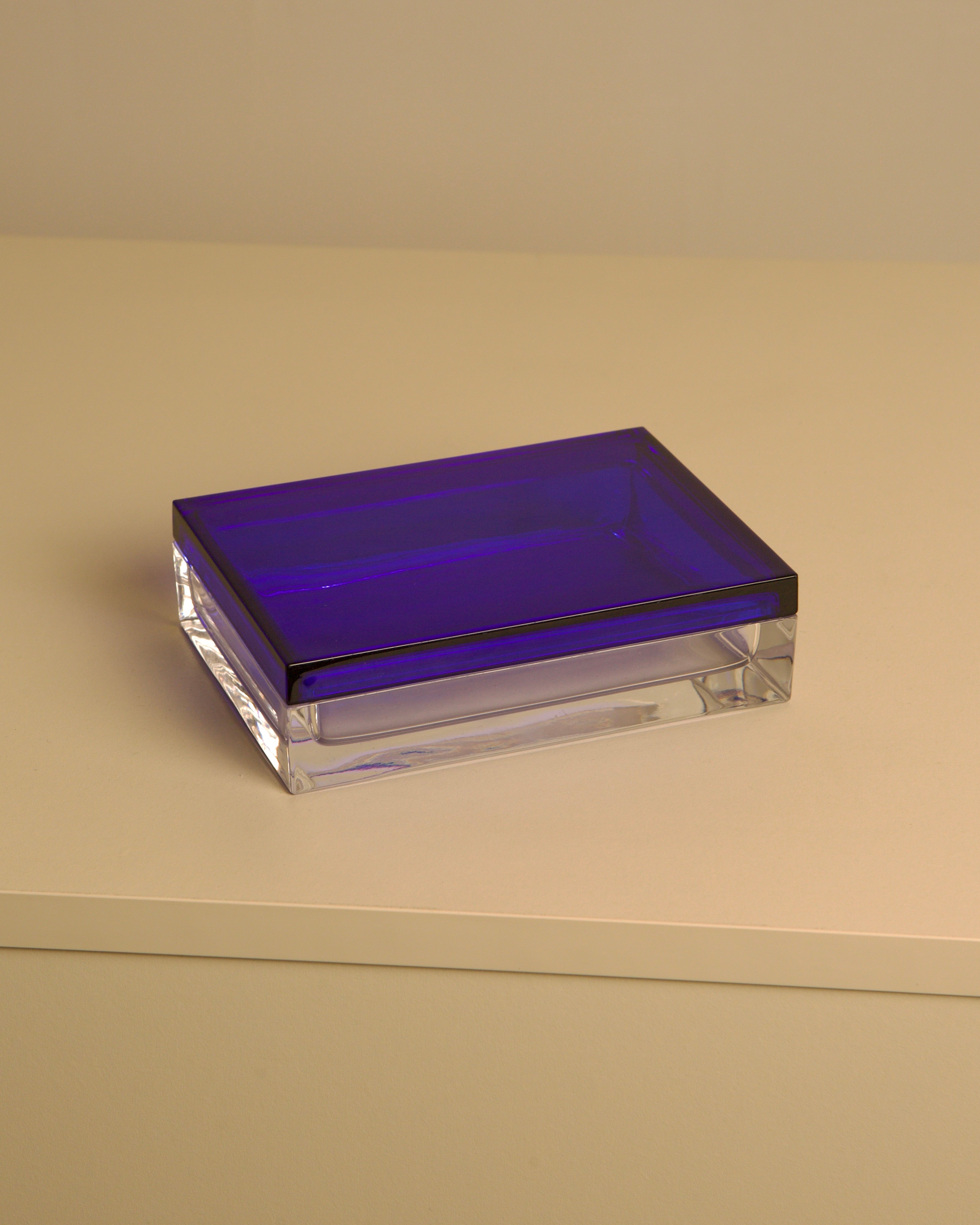The "Italian Box in Transparent and Blue Crystal by Duccio Di Segna 80's" by Treaptyque features a deep blue lid and clear base, reflecting 1980s Italian design. It rests on a light surface with a beige backdrop.