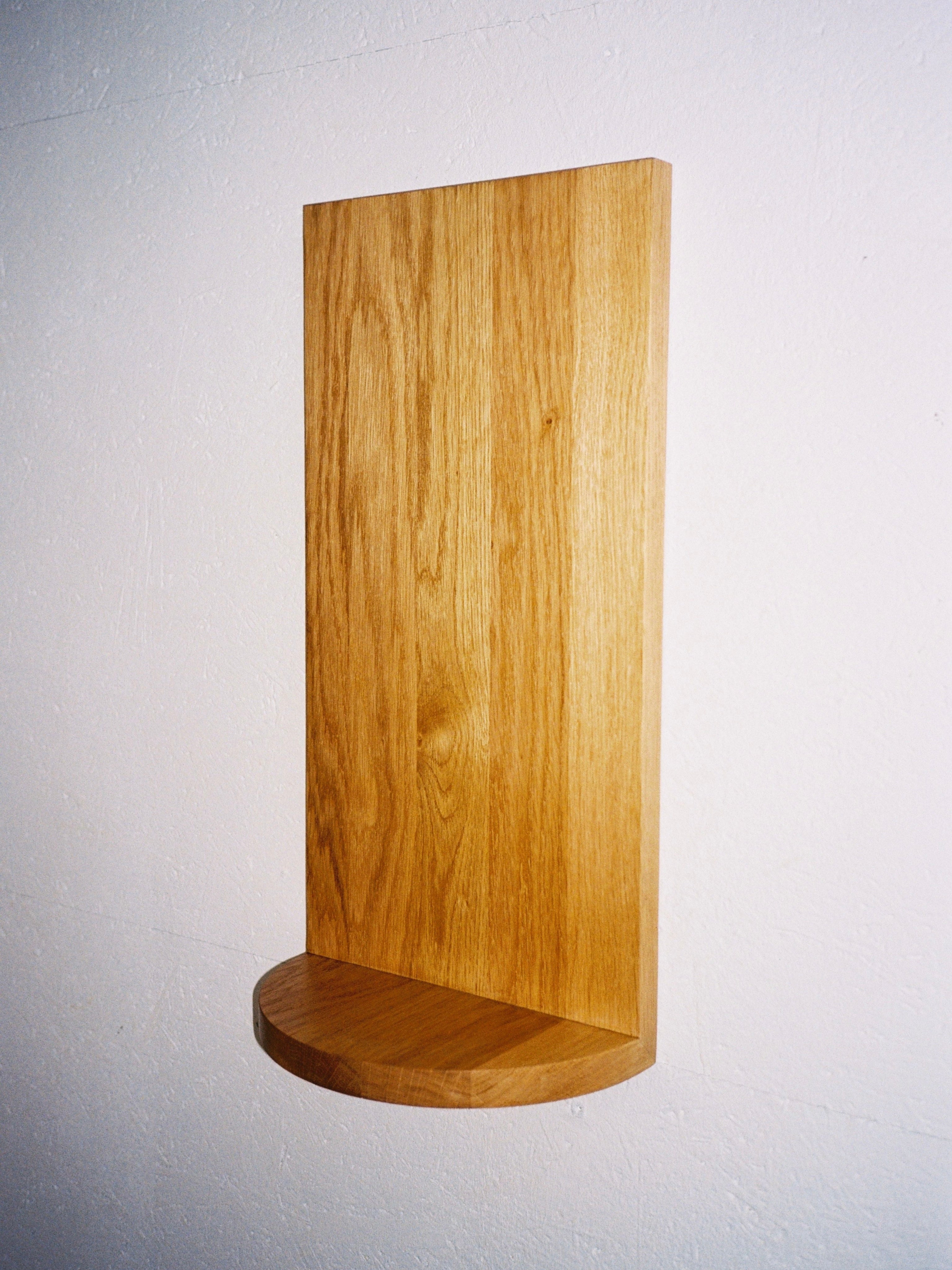 The Megaron - Minimalist Shelf in Wood - Small by COSEINCORSO is a handcrafted solid oak shelf featuring a rectangular back panel and a small, semi-circular base, elegantly mounted on a white wall.