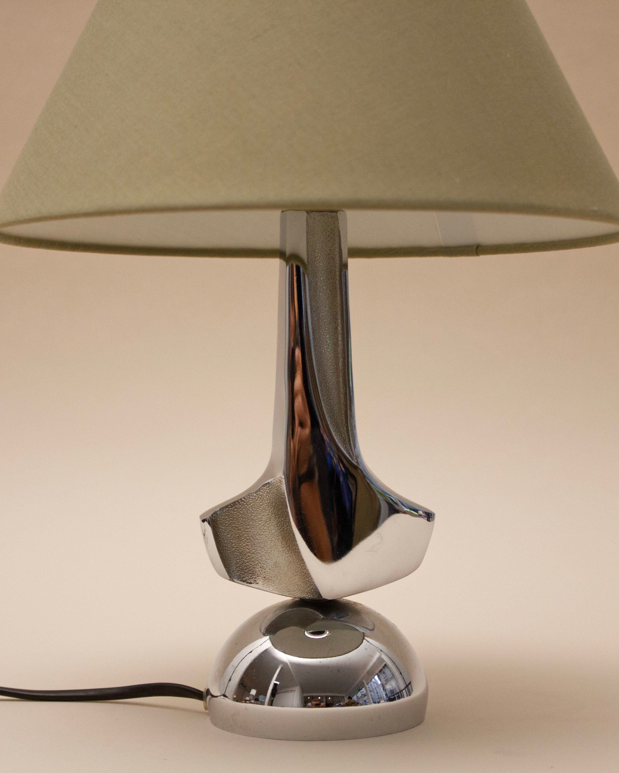 The SÒLER MELLILA Table Lamp features a chrome base and beige lampshade, offering a modern look against a plain light background. Its cord is visible at the bottom left.