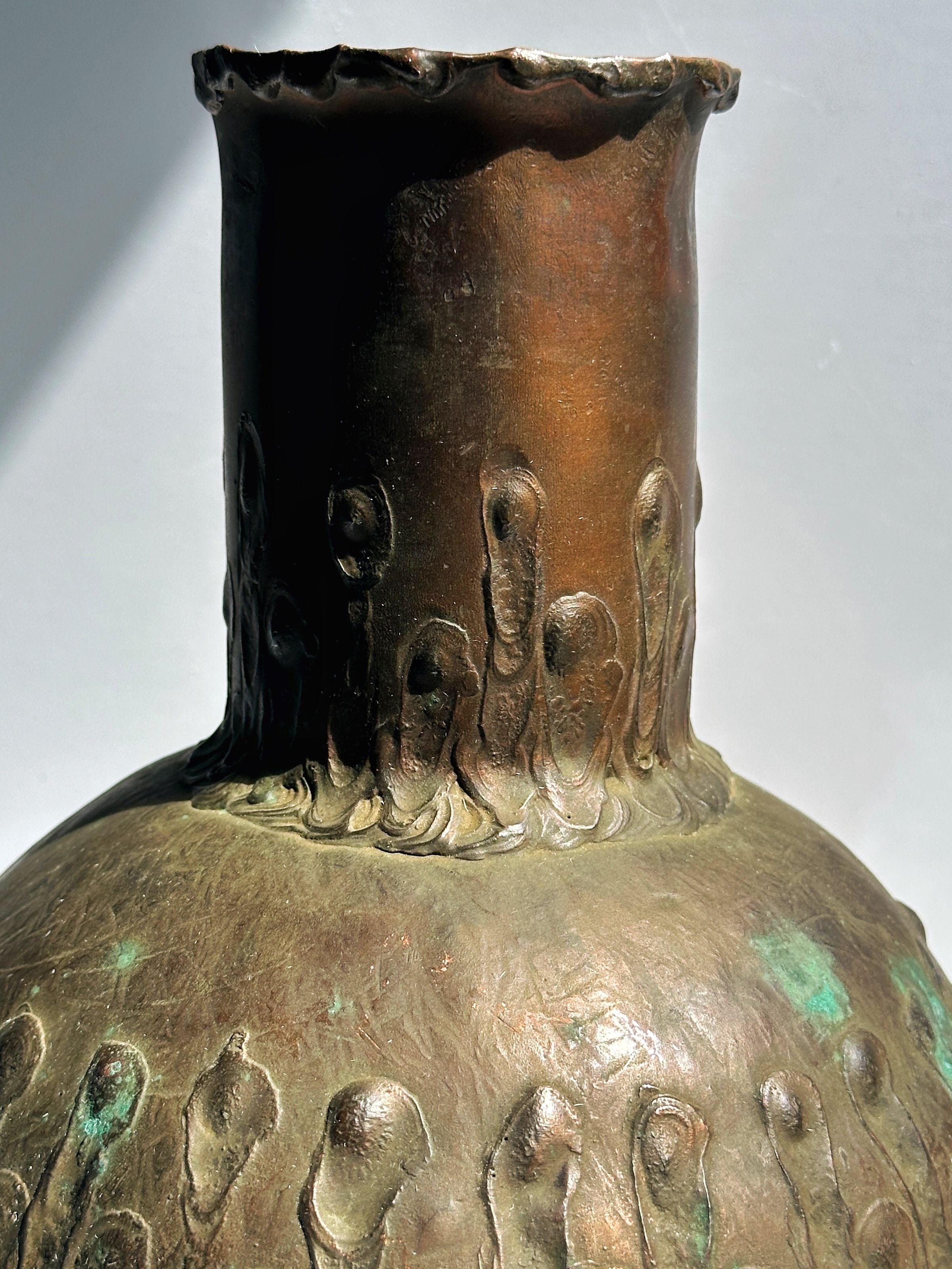 Copper vase neck detail showing decorative relief patterns and patina