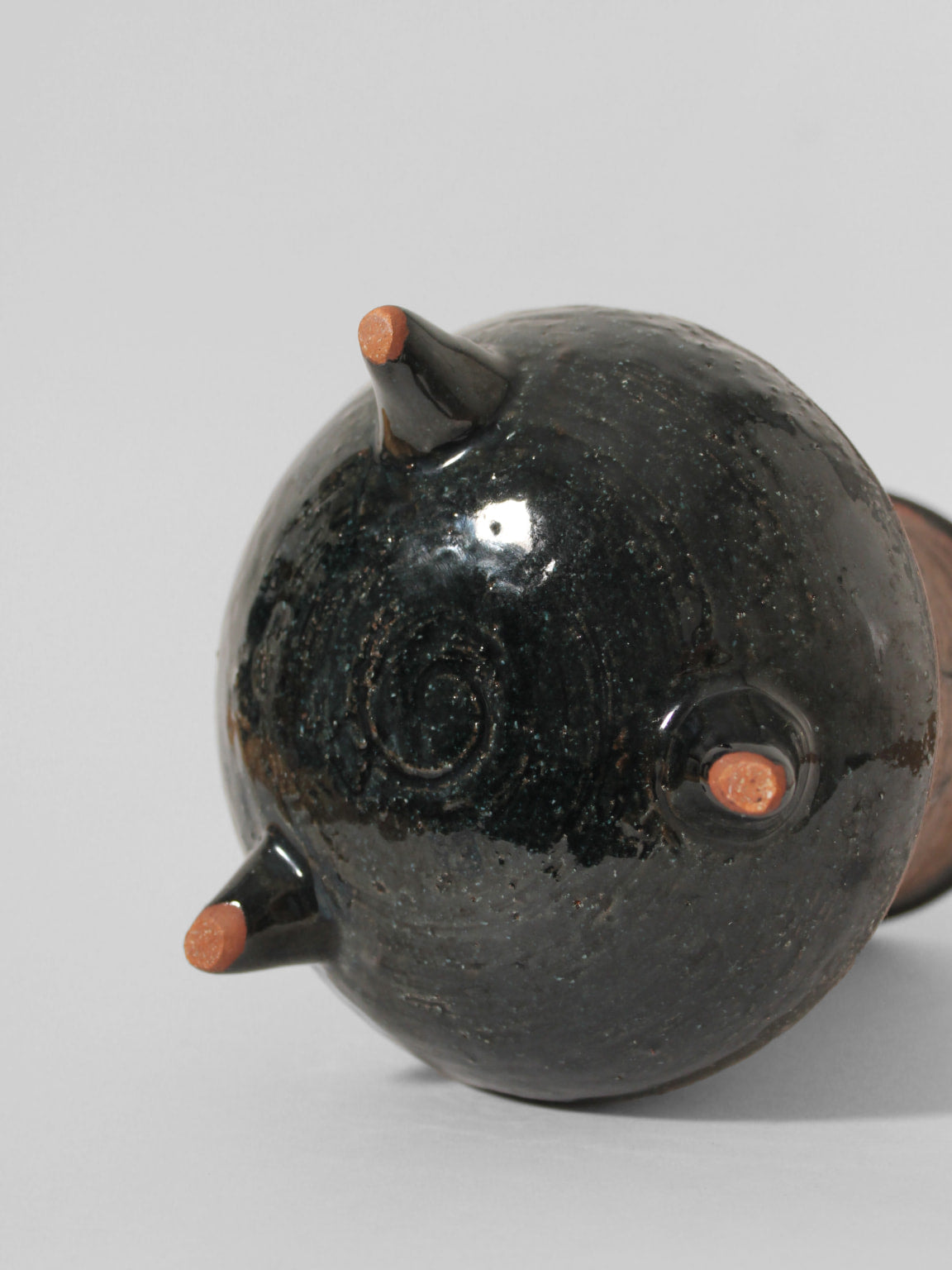 A close-up of the Eke Bjerén Ceramic Vase On Legs, made for Gabriel Sweden in the 1960s by Vintage Stories, featuring a dark glossy body with three conical legs and unglazed reddish-brown tips, shown lying on its side against a light gray background.