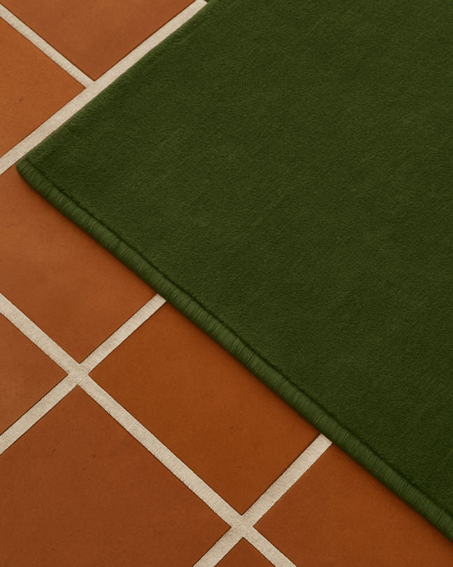 Rug 100% Wool New Zealand - Forest green — side angle on terracotta tiles