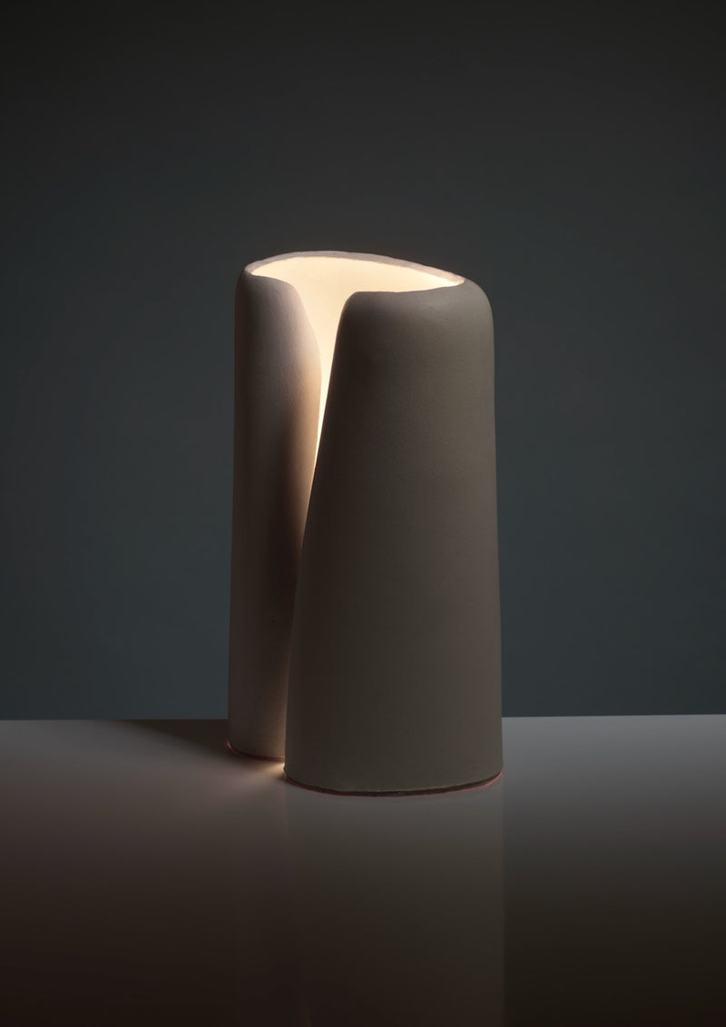 The Snail Table Lamps in Ceramic by Katia Langeard feature a modern, minimalist split design with a soft matte finish, casting warm light from the top—ideal as chic bedside lamps against dark decor.