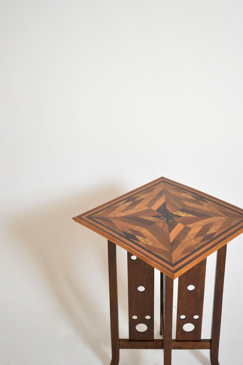 The Geometric Marquetry Side Table, 1920s by Barracuda Interiors features a striking inlaid star pattern on the square top and decorative circular cutouts on the legs, showcased against a plain white background.